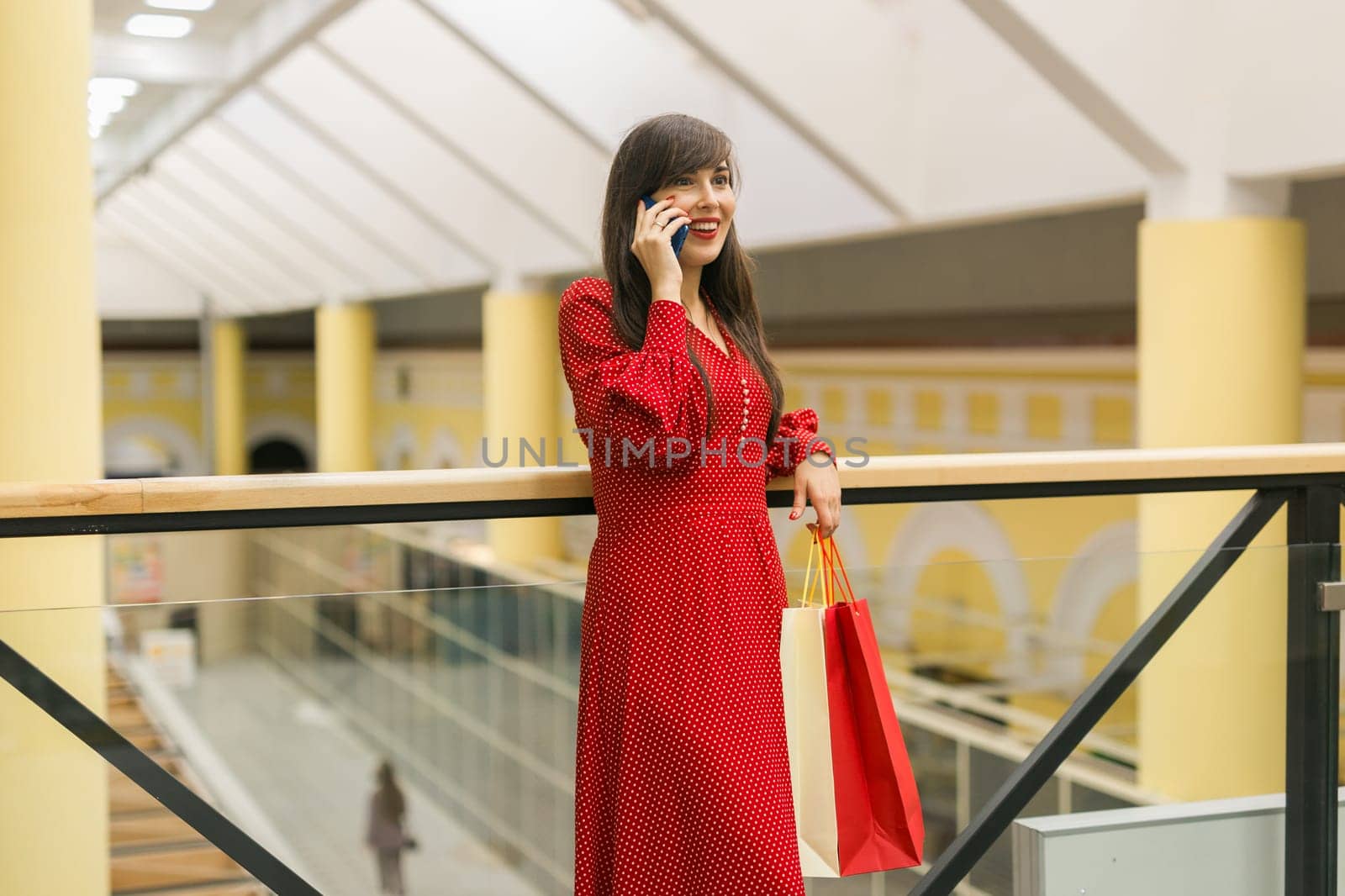 Woman talks on phone while shopping in mall. Communication and joy during shopping moments indoors.