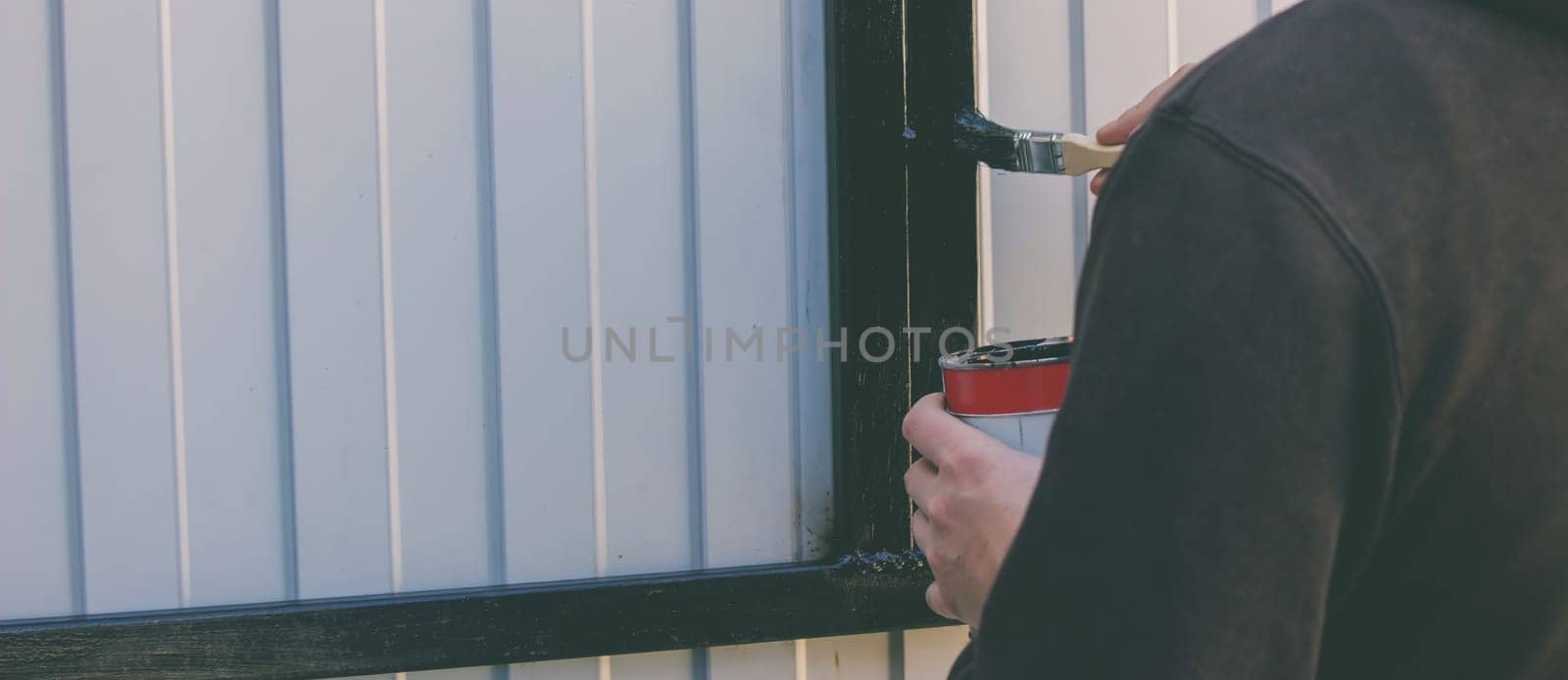 close-up of a man painting metal black with a brush.painting