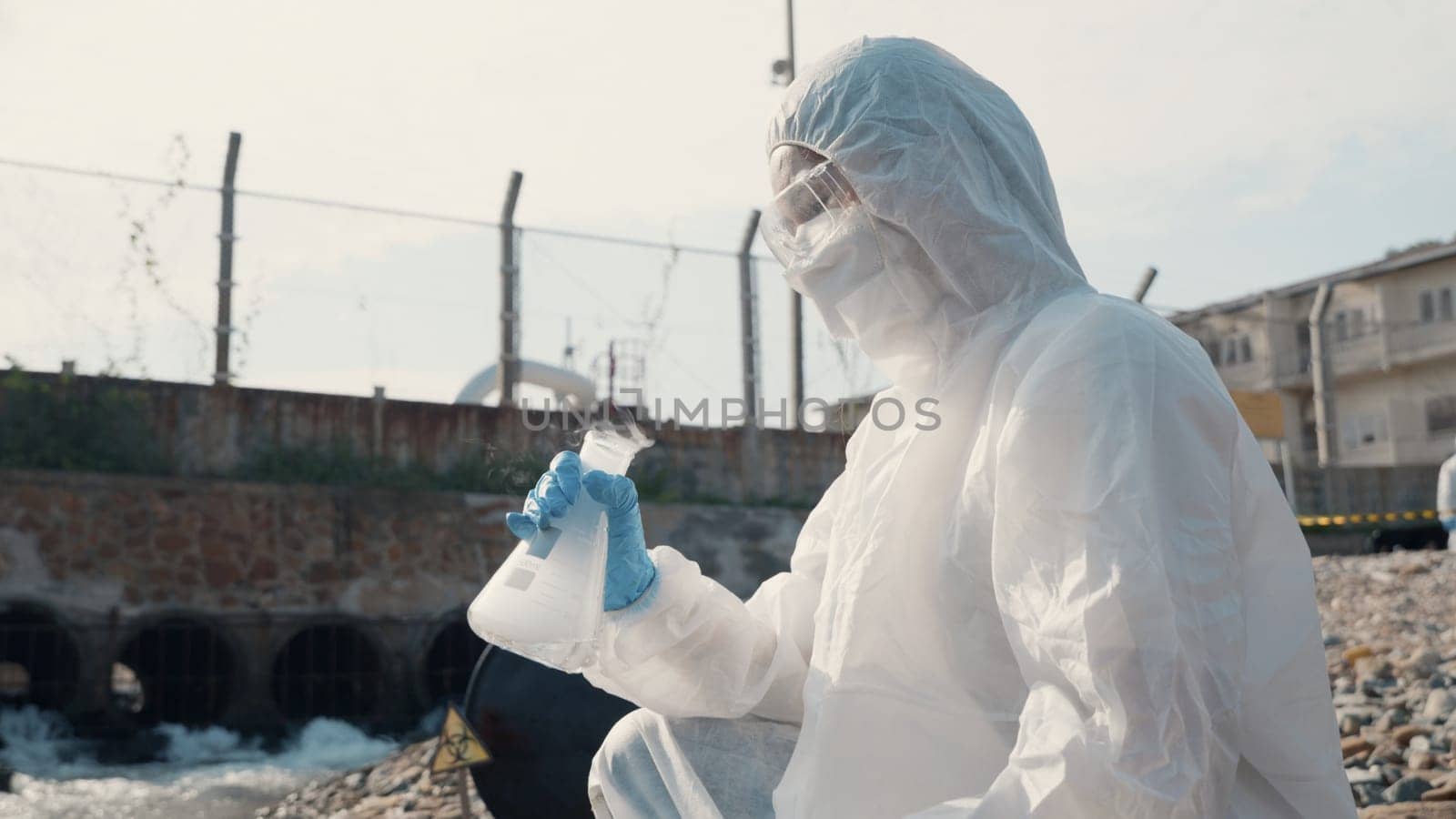 Ecologist sampling water toxic chemicals from river with test tube glass and have white smoke, Biologist wear protective suit and mask collects sample waste water from industrial, problem environment