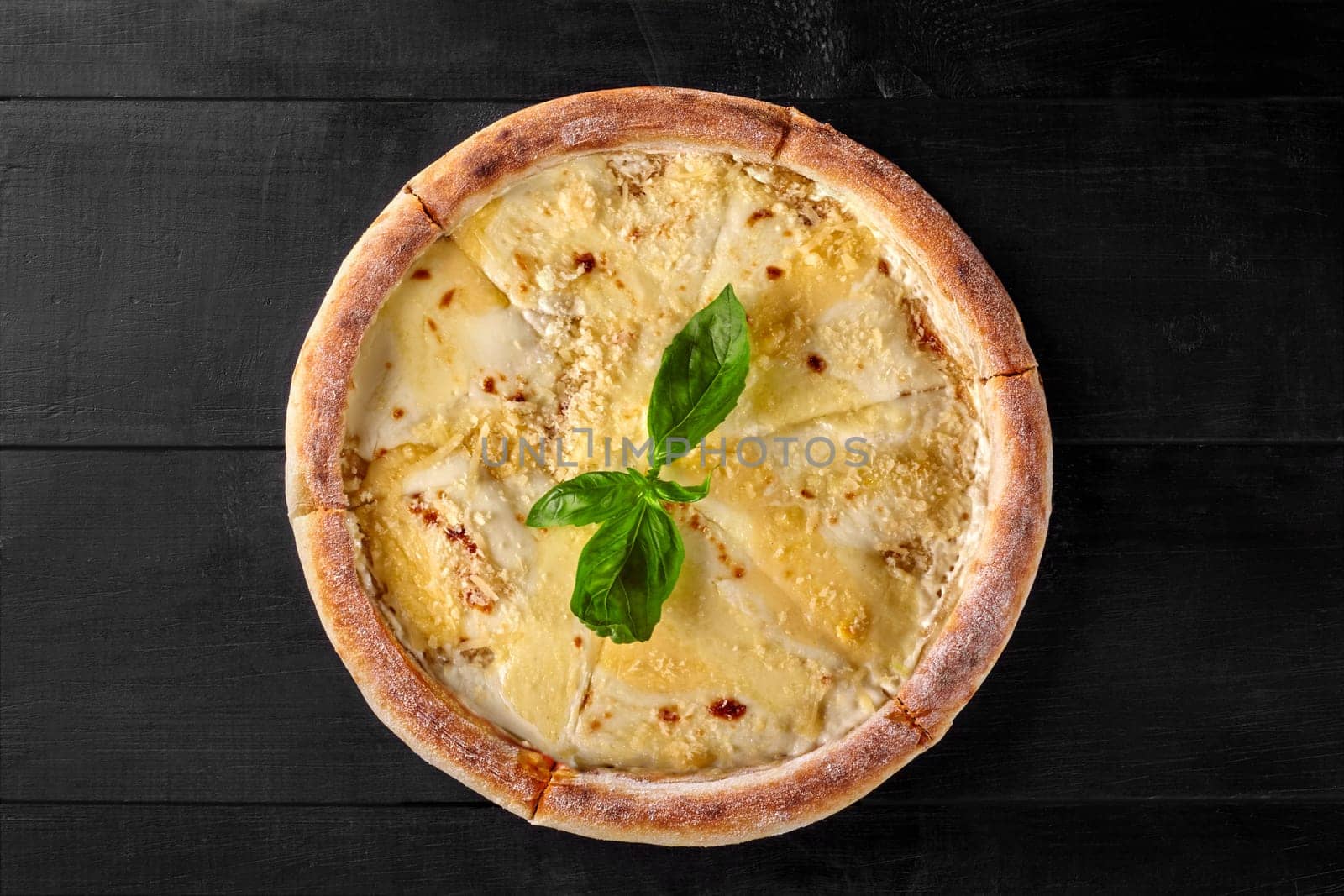 Four cheese pizza with basil topping on a black wooden table, representing italian cuisine
