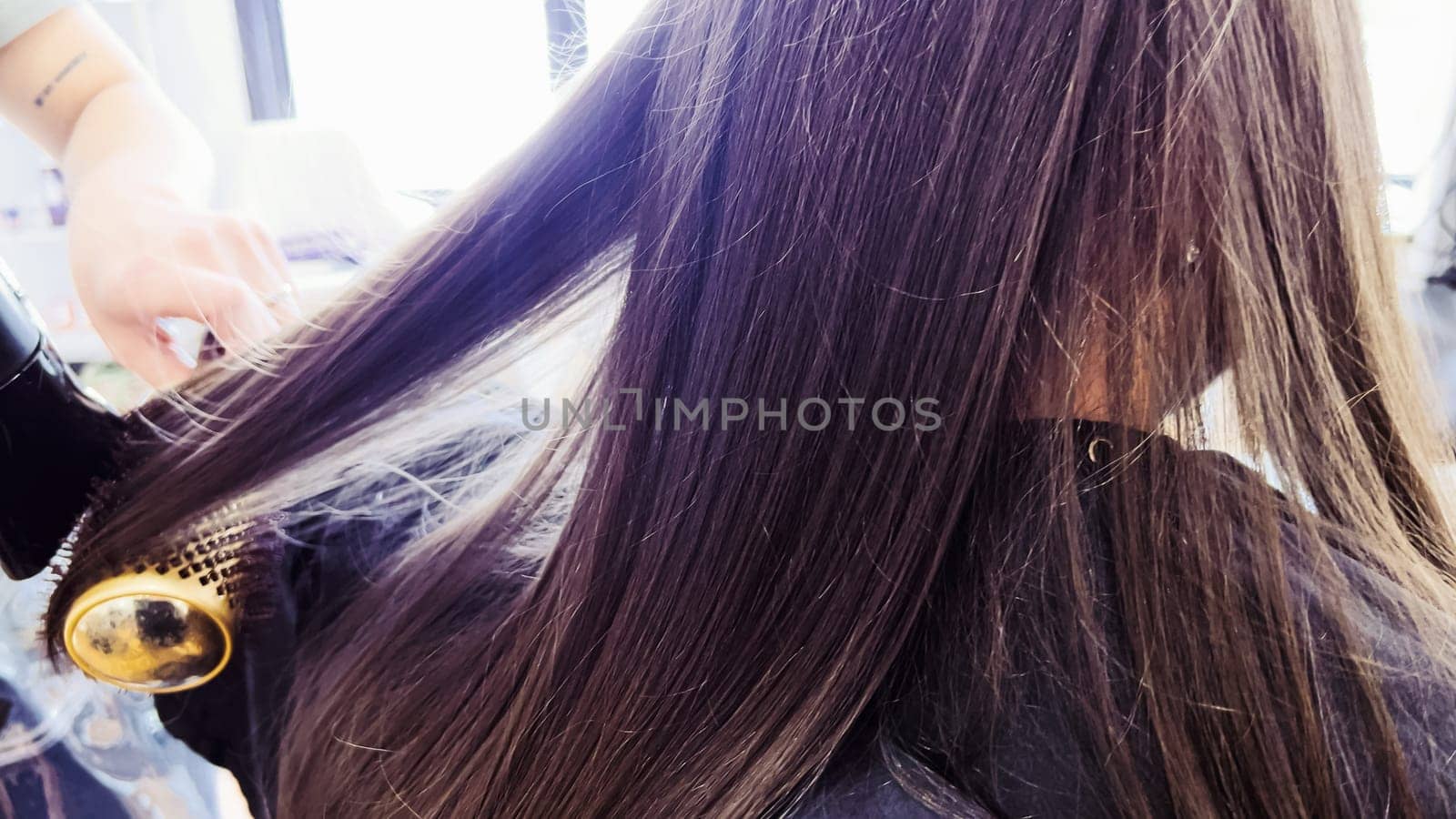 Gentle hands maneuver a hair dryer through a young girl's newly cut hair, showcasing the drying process after a meticulous trim. The warmth of the dryer breathes life into her locks, as they transform from damp to styled with care and expertise.