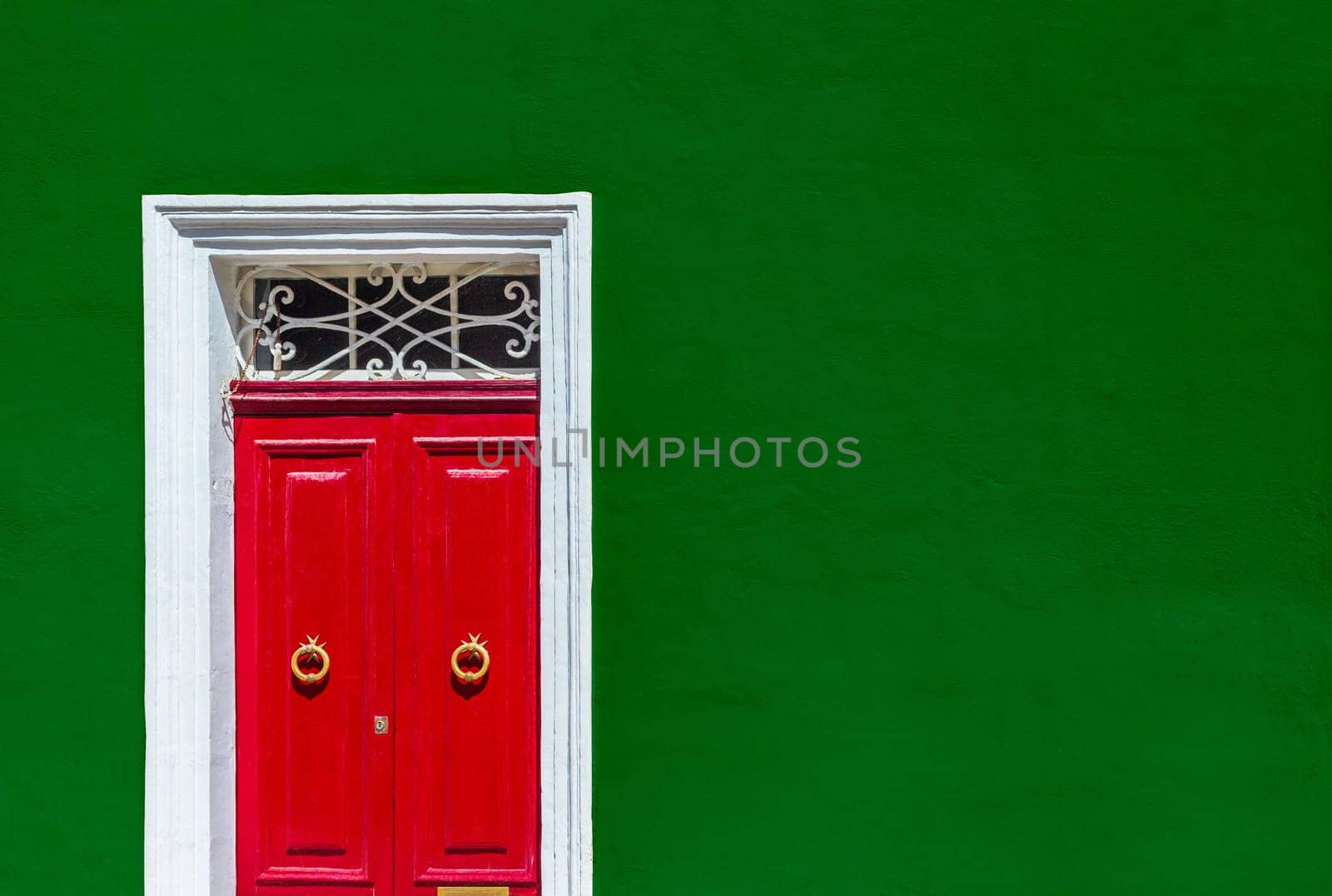 Green wall of a residential building with a red door in a white wooden frame