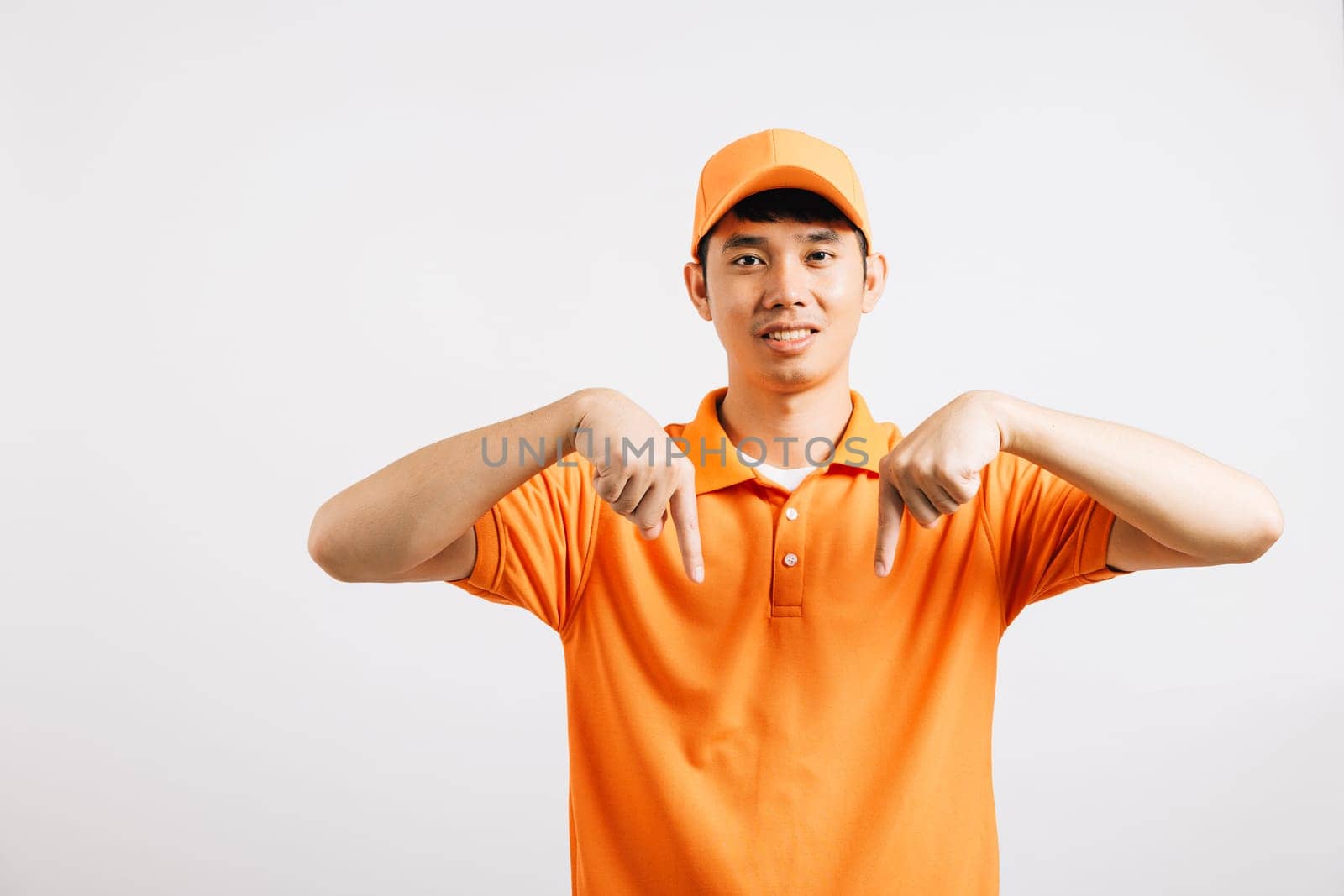 Portrait Asian smiling young delivery man pointing down something with empty space hands studio isolated white background, Happy lifestyle men carry person in an orange shirt uniform point finger