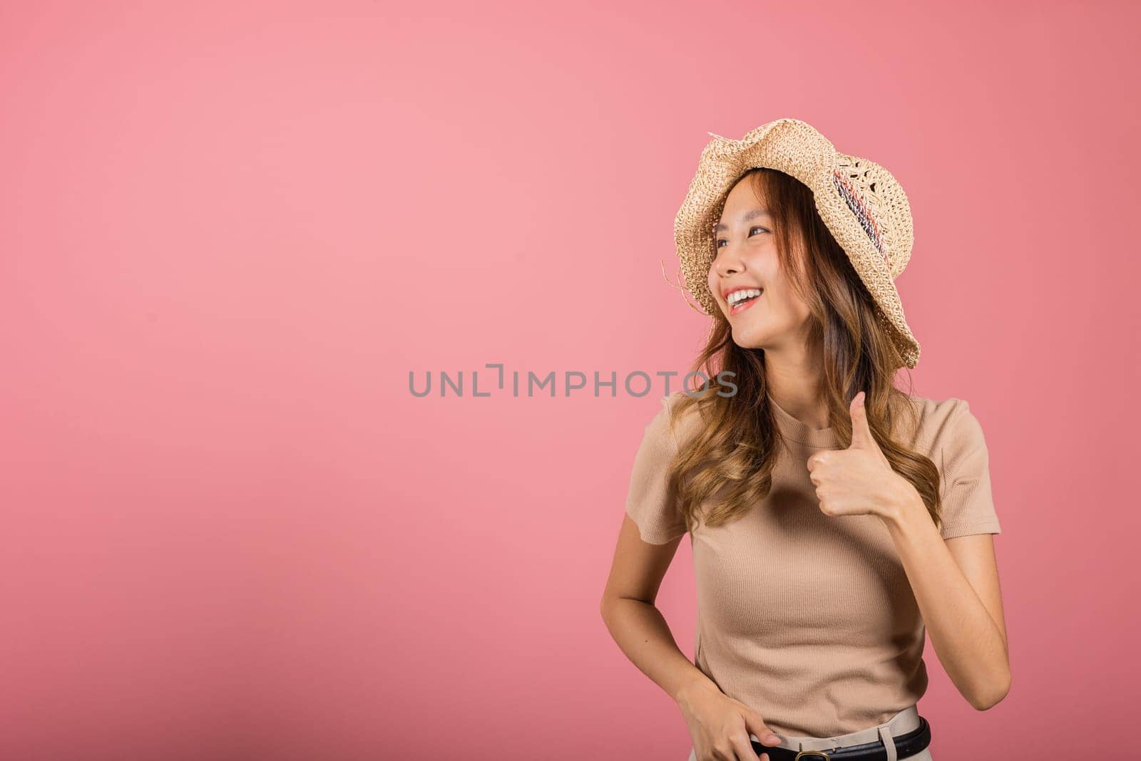 Portrait Asian young woman is smiling and giving a thumbs up while wearing a hat in studio shot isolated pink background, which gives it a cheerful and positive vibe, excellent sign