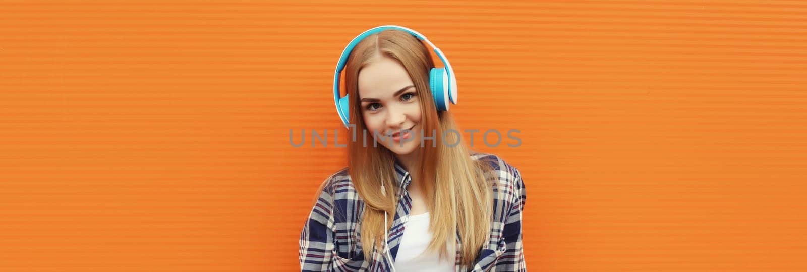 Summer portrait of happy modern young woman listening to music with headphones on orange wall background