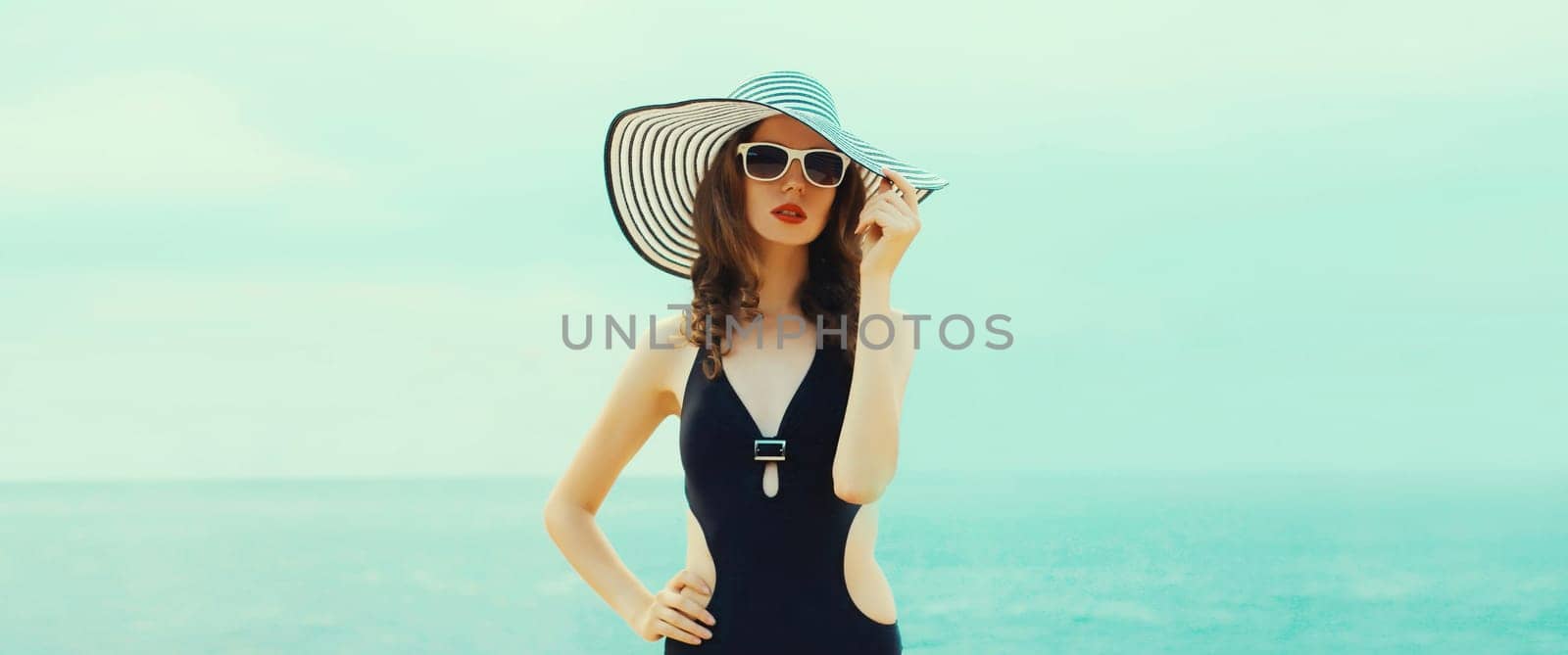 Summer vacation, beautiful young woman in bikini swimsuit and black straw tourist hat, stylish girl posing on the beach on sea coast background