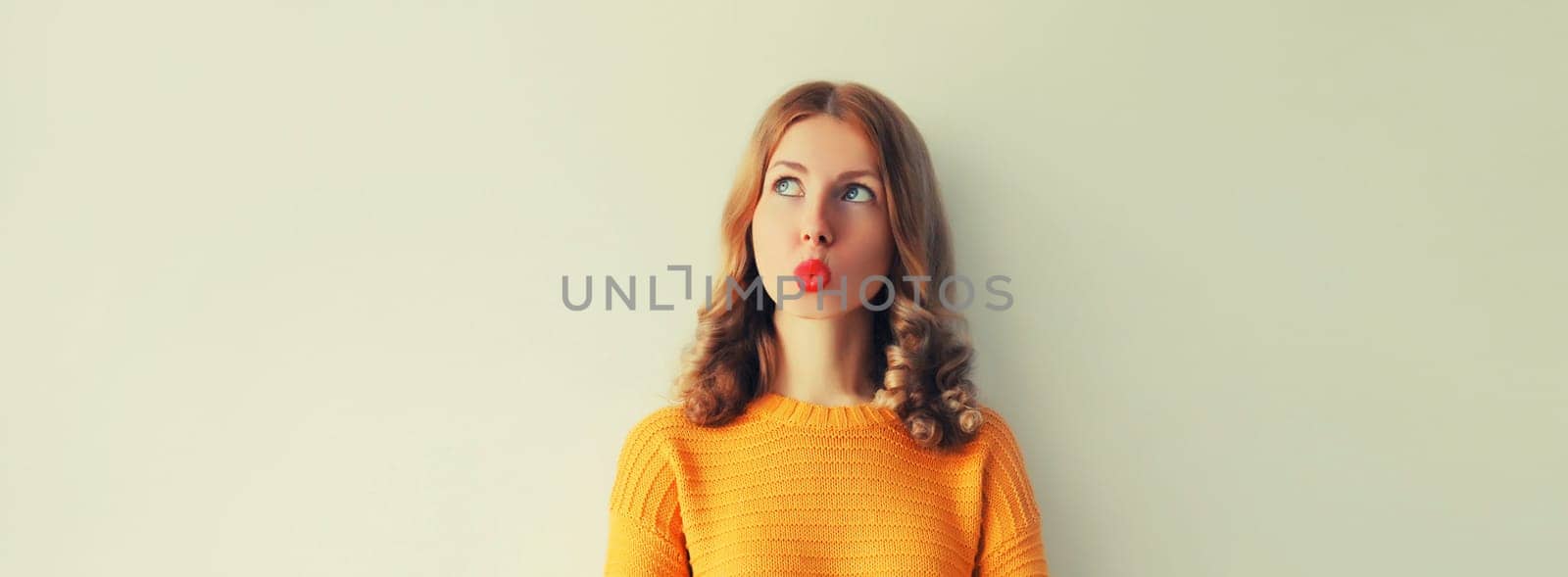 Pensive caucasian young woman thinks looking away, red lipstick, on studio background, blank copy space