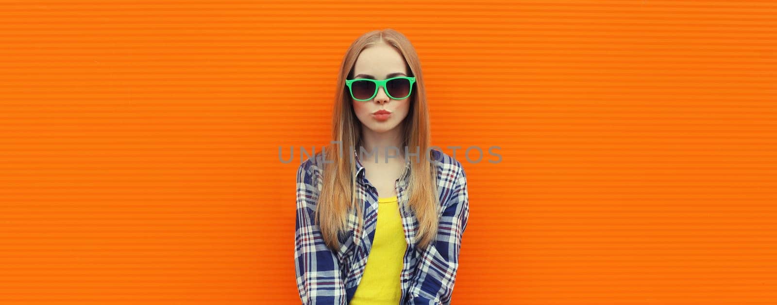 Summer portrait of happy cheerful stylish young woman, teenager girl in colorful clothes, glasses posing on orange background on city street