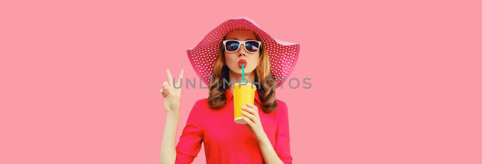 Summer portrait of beautiful young woman drinking fresh juice wearing straw hat, pink dress on studio background