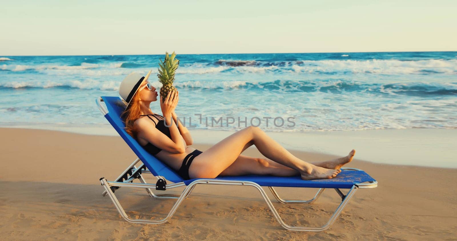 Summer vacation, happy young woman lying on deckchair with pineapple on the beach on sea background
