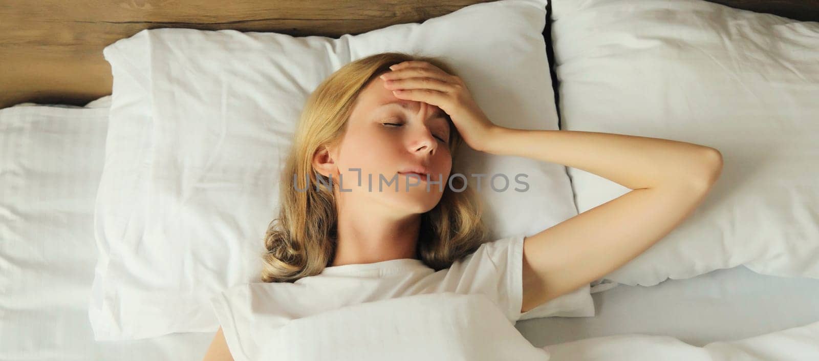 Exhausted tired woman touching head, suffering from headache, stress, fatigue, temples pain, migraine, loud noise, tension lying on the pillow in bed in bedroom at home