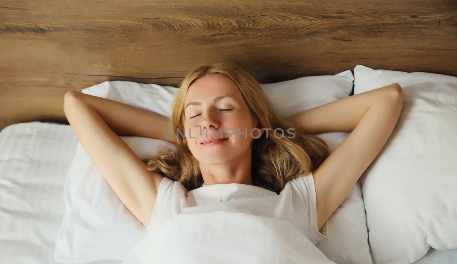 Happy young woman sleeping lying in bed on white soft comfortable pillow in bedroom at home, copy space background