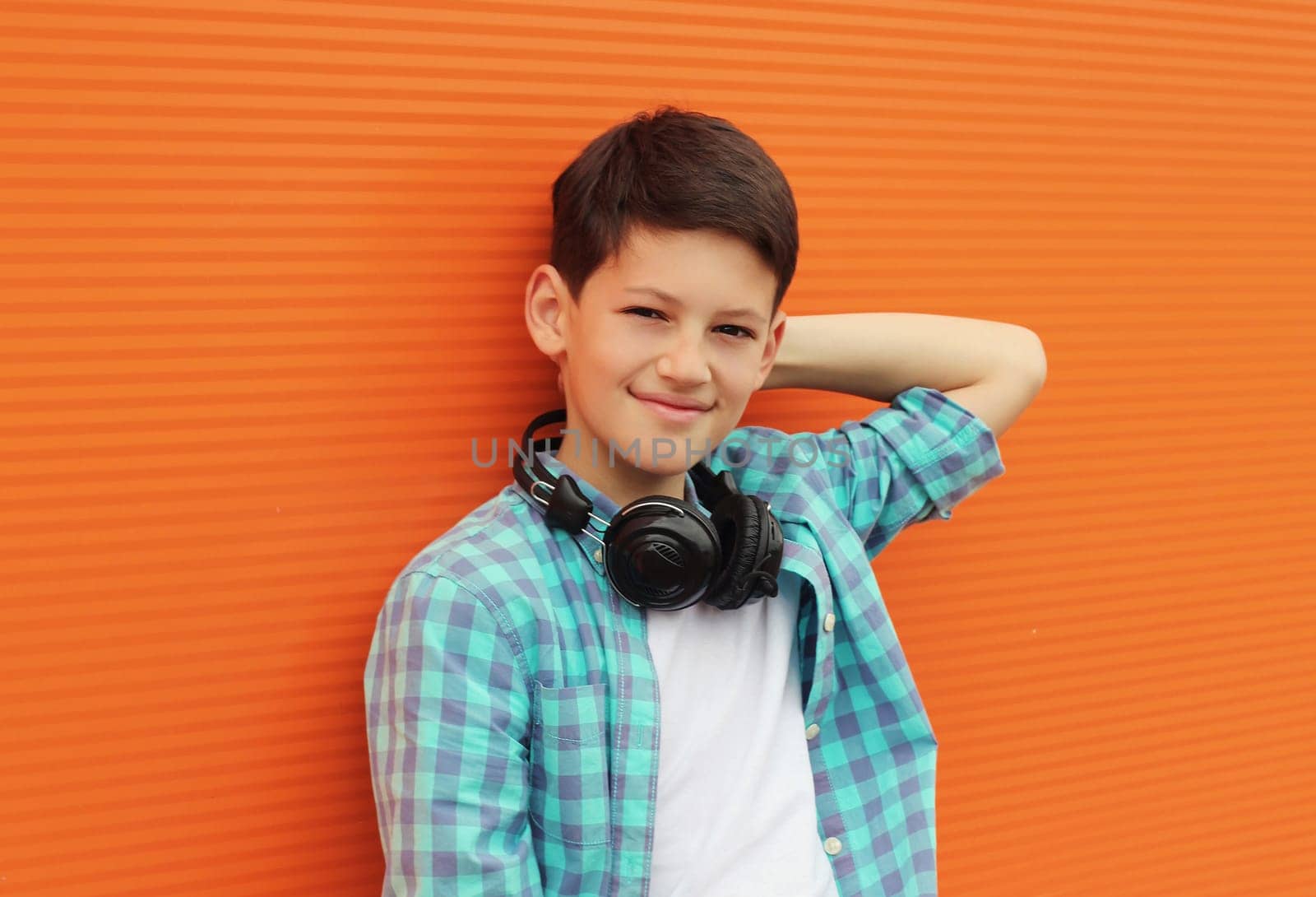 Portrait of happy modern teenage boy listening to music with headphones in the city on orange wall background