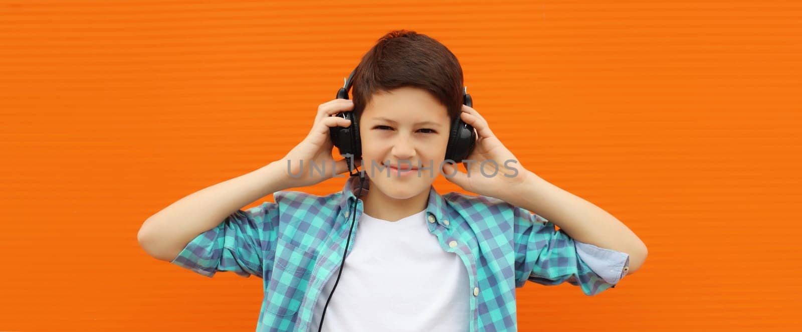 Portrait of happy modern teenage boy listening to music with headphones in the city on orange wall background