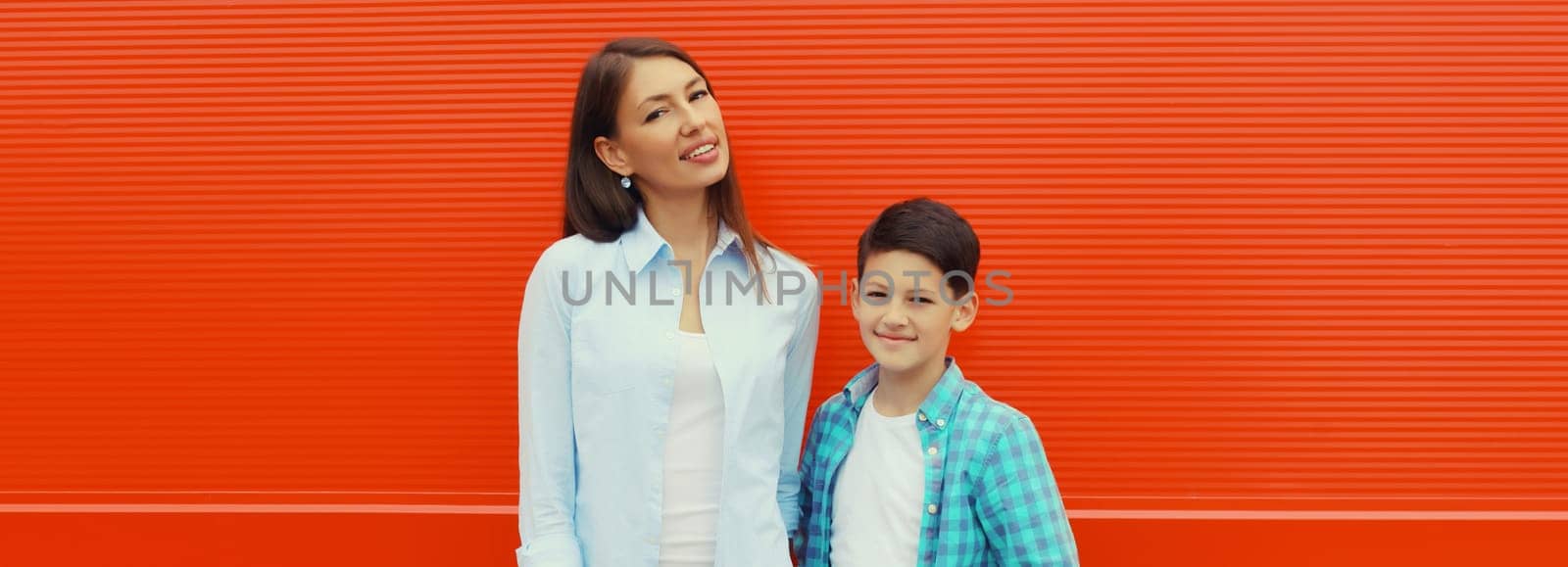 Happy smiling mother with son teenager posing together in casual clothing in the city on orange wall background