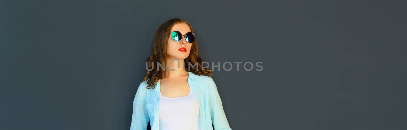 Portrait of stylish modern young woman in glasses, posing on black wall background