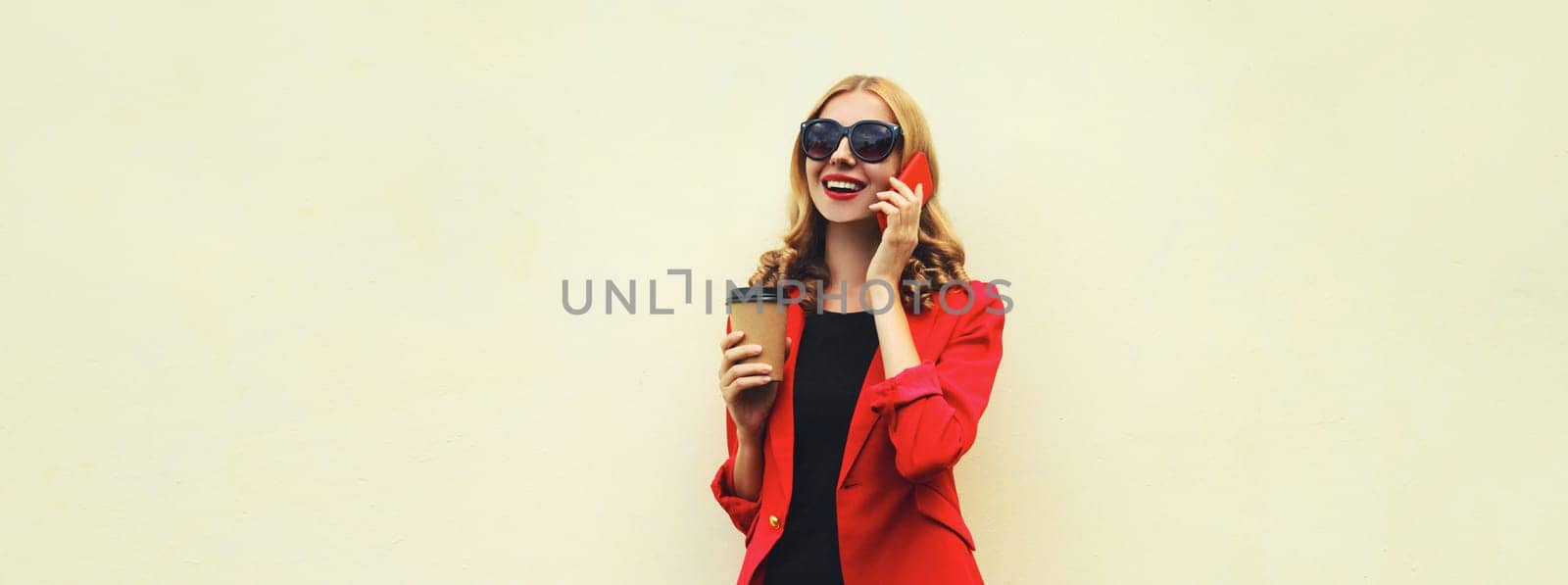 Beautiful young woman calling on smartphone in red business suit with coffee drink cup isolated on white background