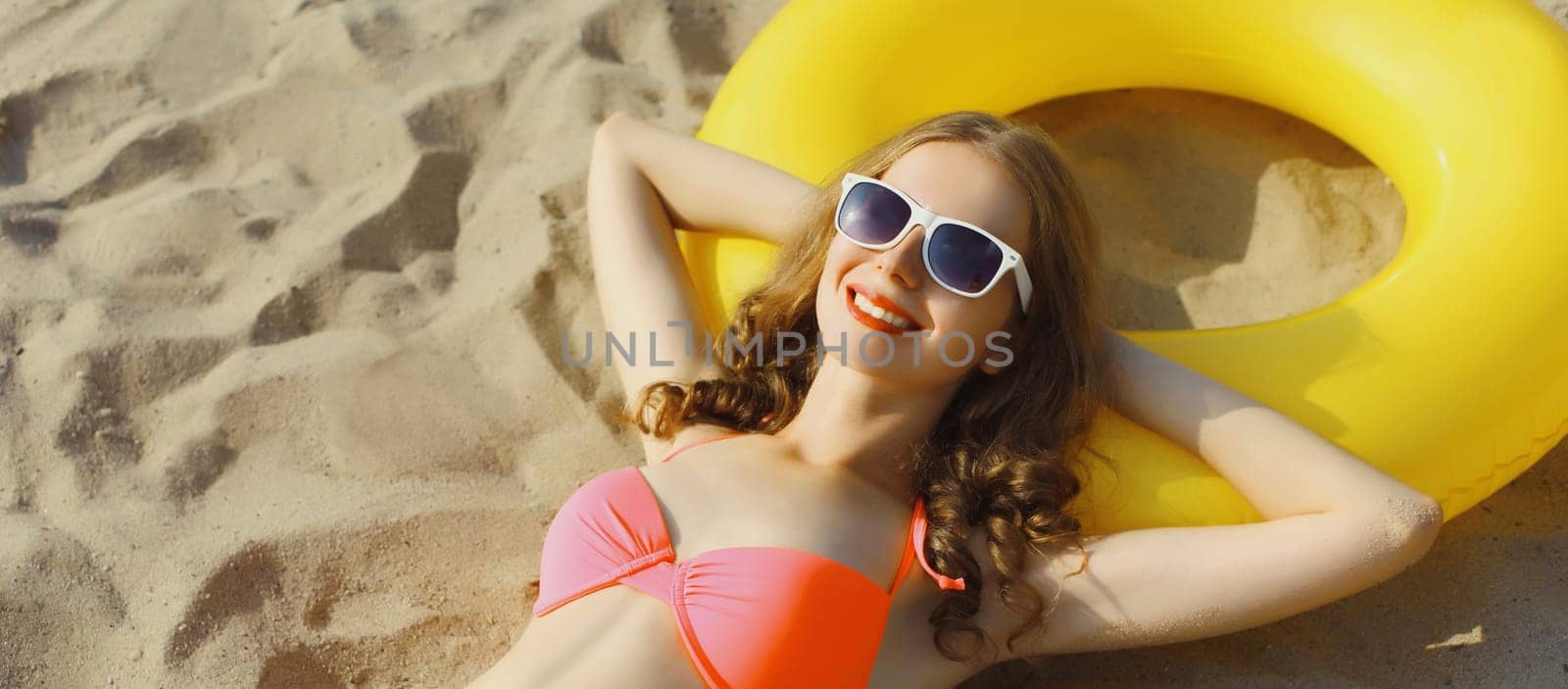 Summer vacation, happy relaxing young woman lying on the sand on the beach with swimming inflatable ring enjoying summer holiday