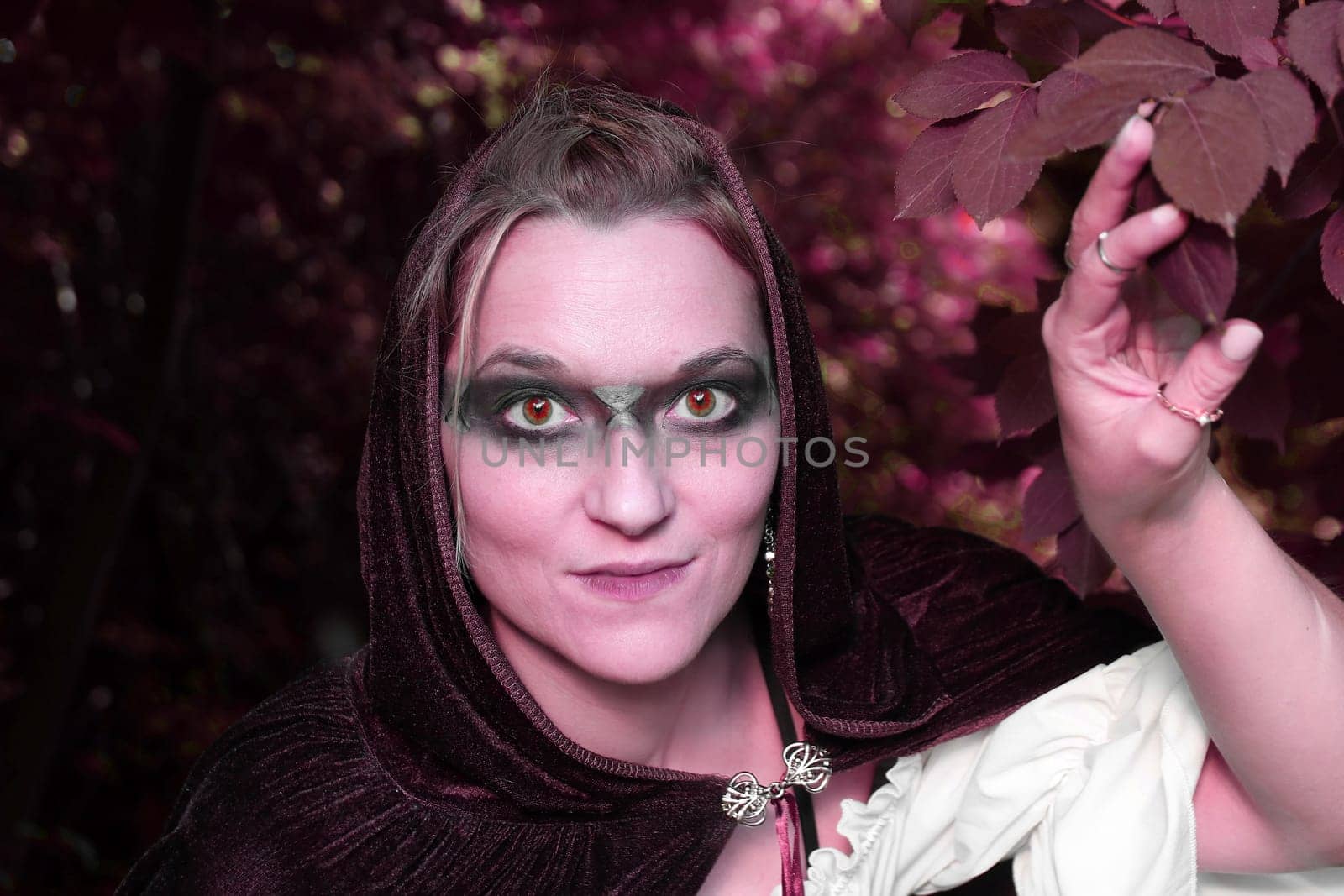 A woman dressed as a red forest spirit or witch looks out of the bushes