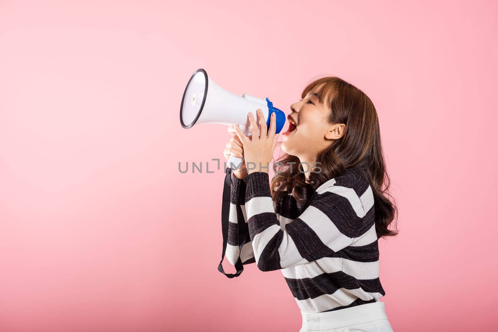Portrait of happy Asian beautiful young woman teen confident smiling face holding making announcement message shouting screaming in megaphone, studio shot isolated on pink background, with copy space