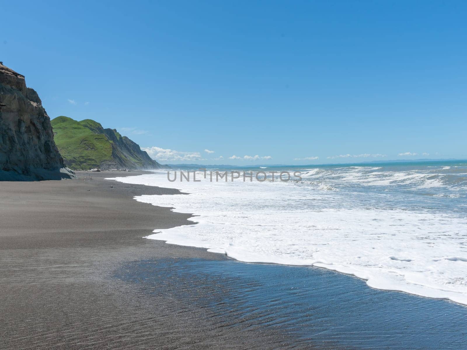 Waves crash onto South Pacific beach lined with cliffs bin New Zealand leading white foam wash as they flow back.