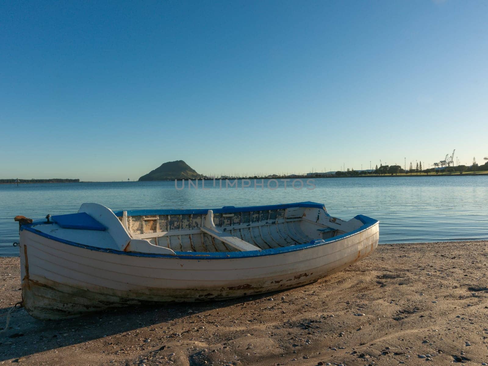 Old blue and white wooden clinker dinghy on beach at mid-tide with landmark Mount Maunganui in background from Tauranga New Zealand.