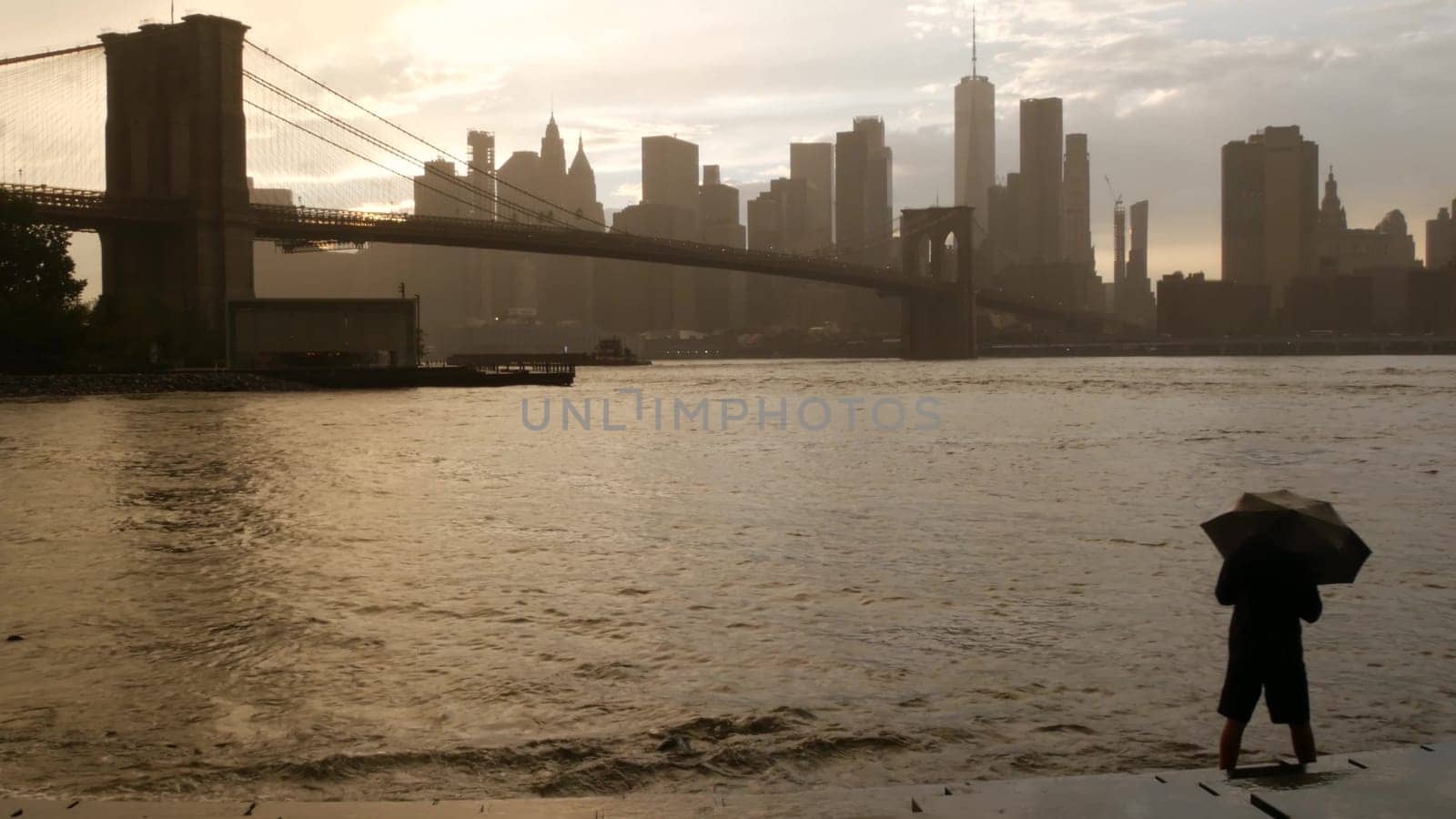 New York City, United States - 11 Sept 2023: Brooklyn Bridge rainy foggy day. Manhattan downtown skyline cityscape, World Trade Center. Man with umbrella, Dumbo Pebble Beach. Autumn river, fall in USA