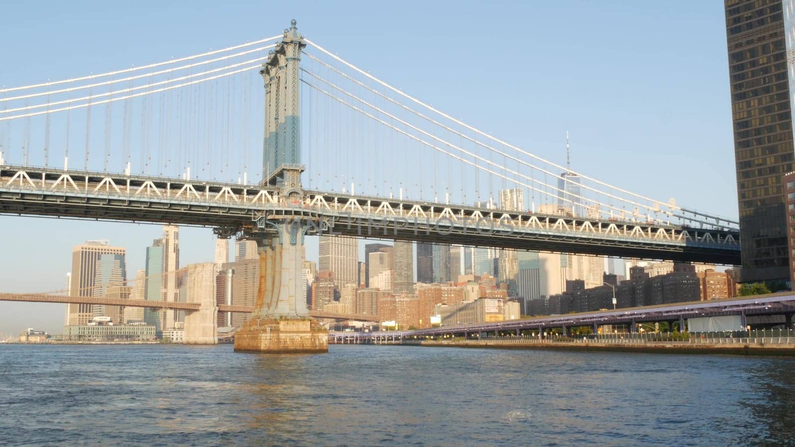 New York City, United States - 7 Sept 2023: Manhattan Bridge to Brooklyn. Waterfront downtown skyline cityscape, financial district skyscrapers from riverfront Pier 35. East river morning sunset.