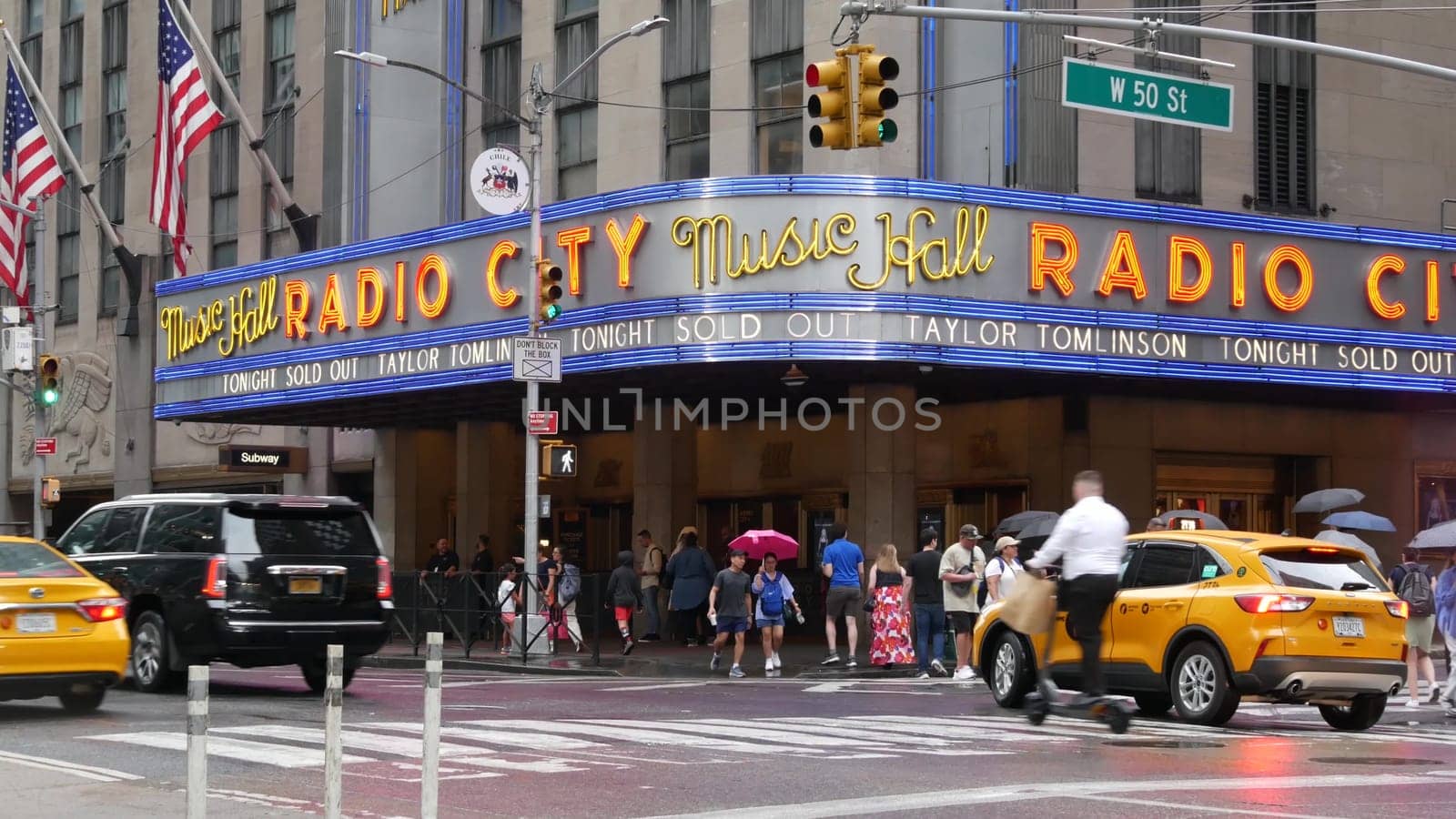 New York, United States - 10 Sept 2023: Manhattan Midtown street. Radio City Music Hall, Rockefeller Center, USA. People pedestrian, urban traffic, 6 Sixth Americas avenue crossroad, yellow taxi cab.