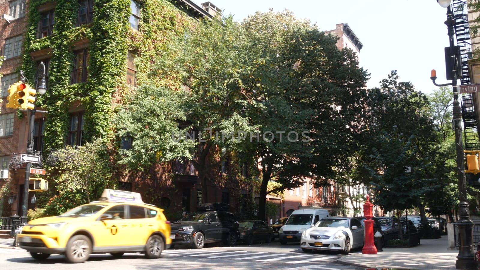 New York City, United States, 6 Sept 2023: Manhattan Midtown Irving street corner, crossroad intersection, Gramercy, USA. People pedestrians. Yellow taxi. Red brick house wall covered ivy plant leaves