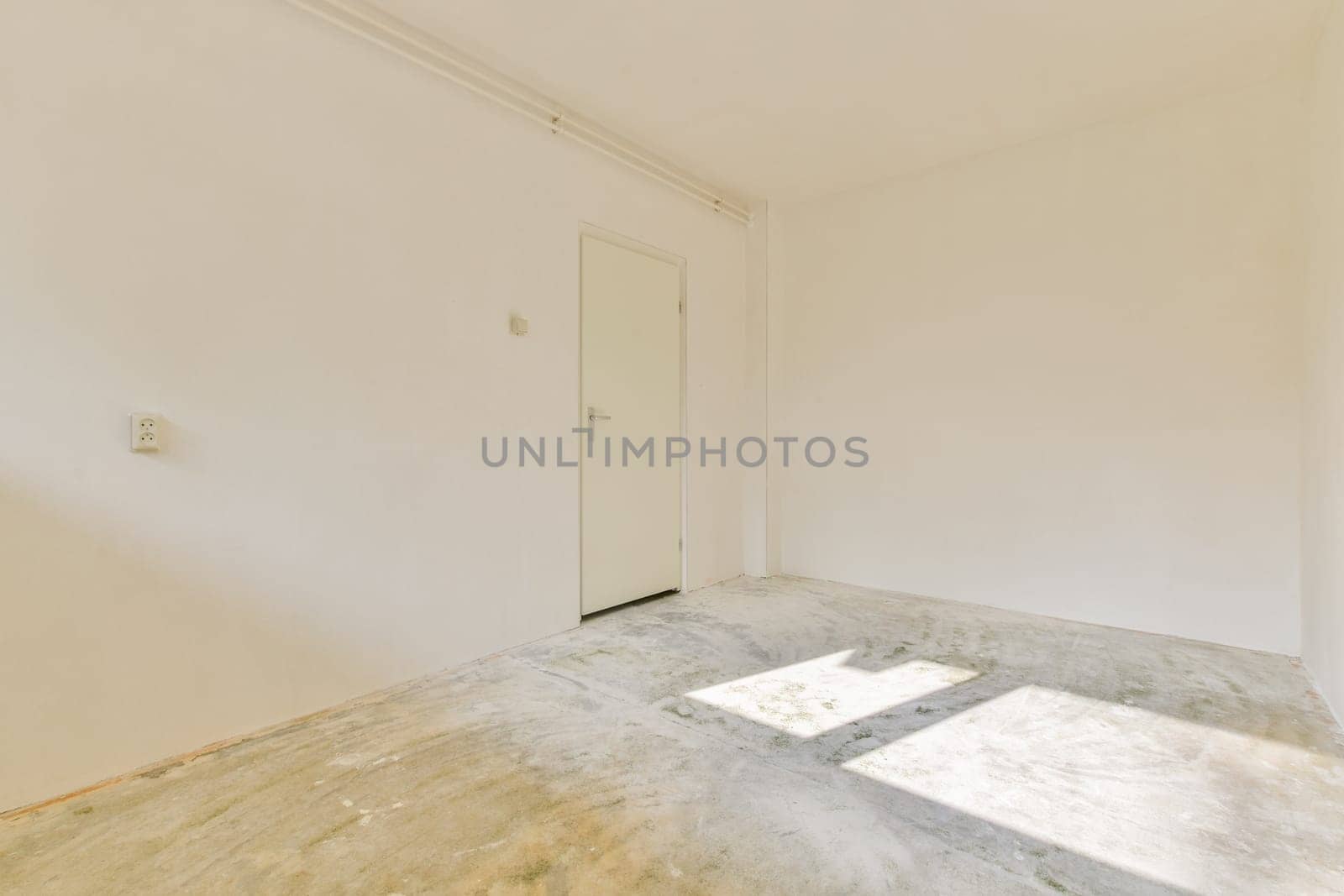 A bright and airy empty room featuring bare walls, a door, and sunlight casting shadows on the floor, creating a serene, minimalist space.