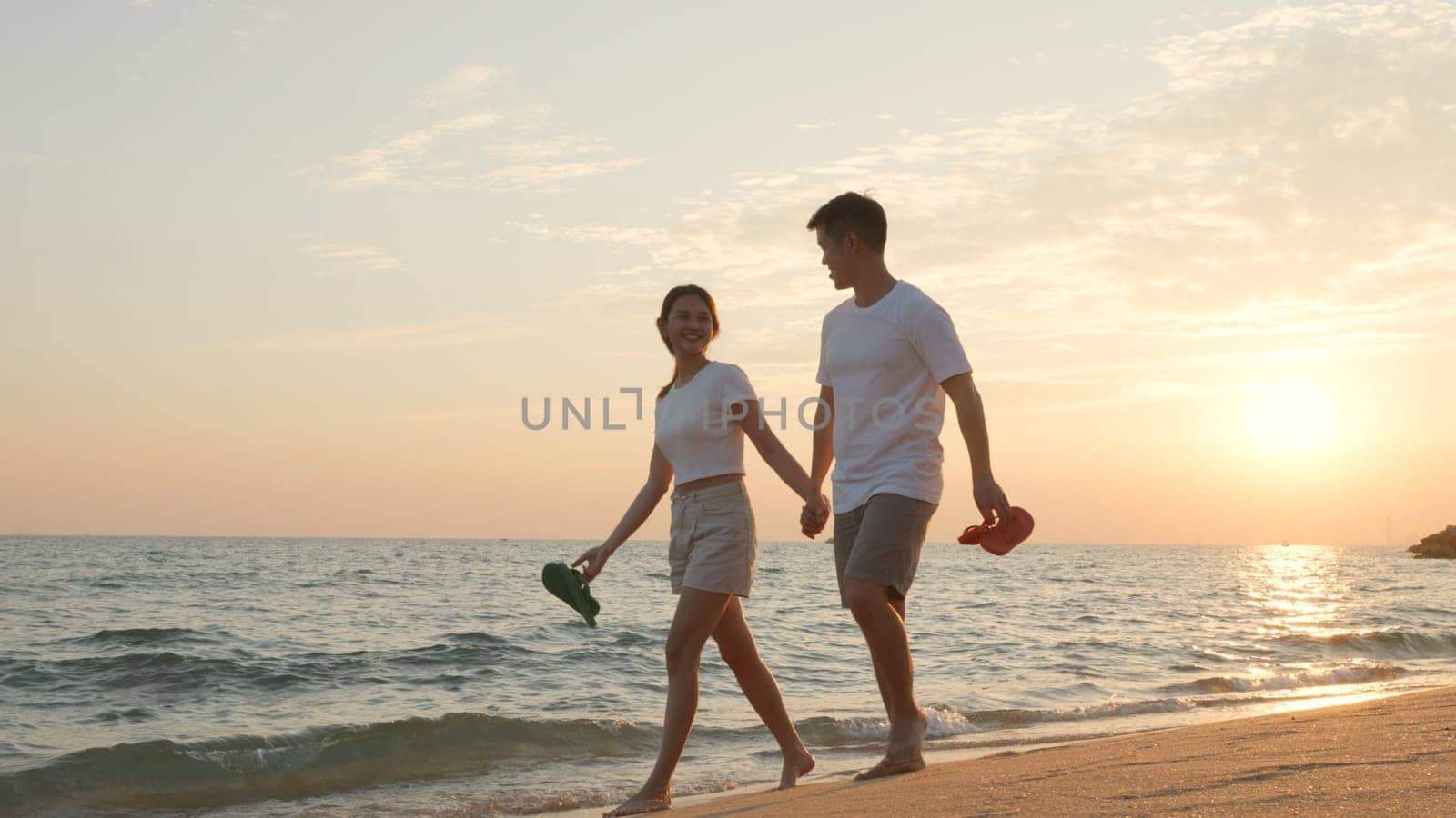 Vacation loving couple walking on beach together at sunset landscape, relaxing vacation travel summer, Asian man and woman in love holding hands walks along the sandy seashore