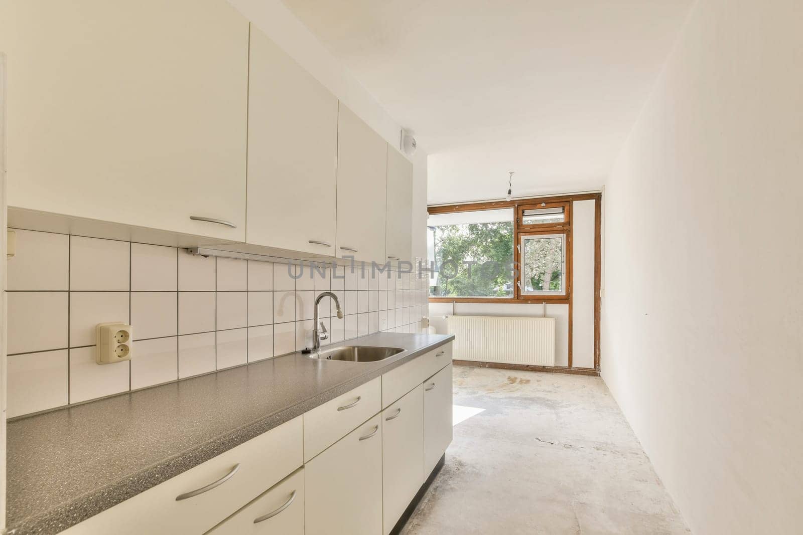 A minimalist kitchen featuring sleek cabinetry, a spacious countertop, and large windows allowing natural light to fill the room. The atmosphere is inviting and modern.