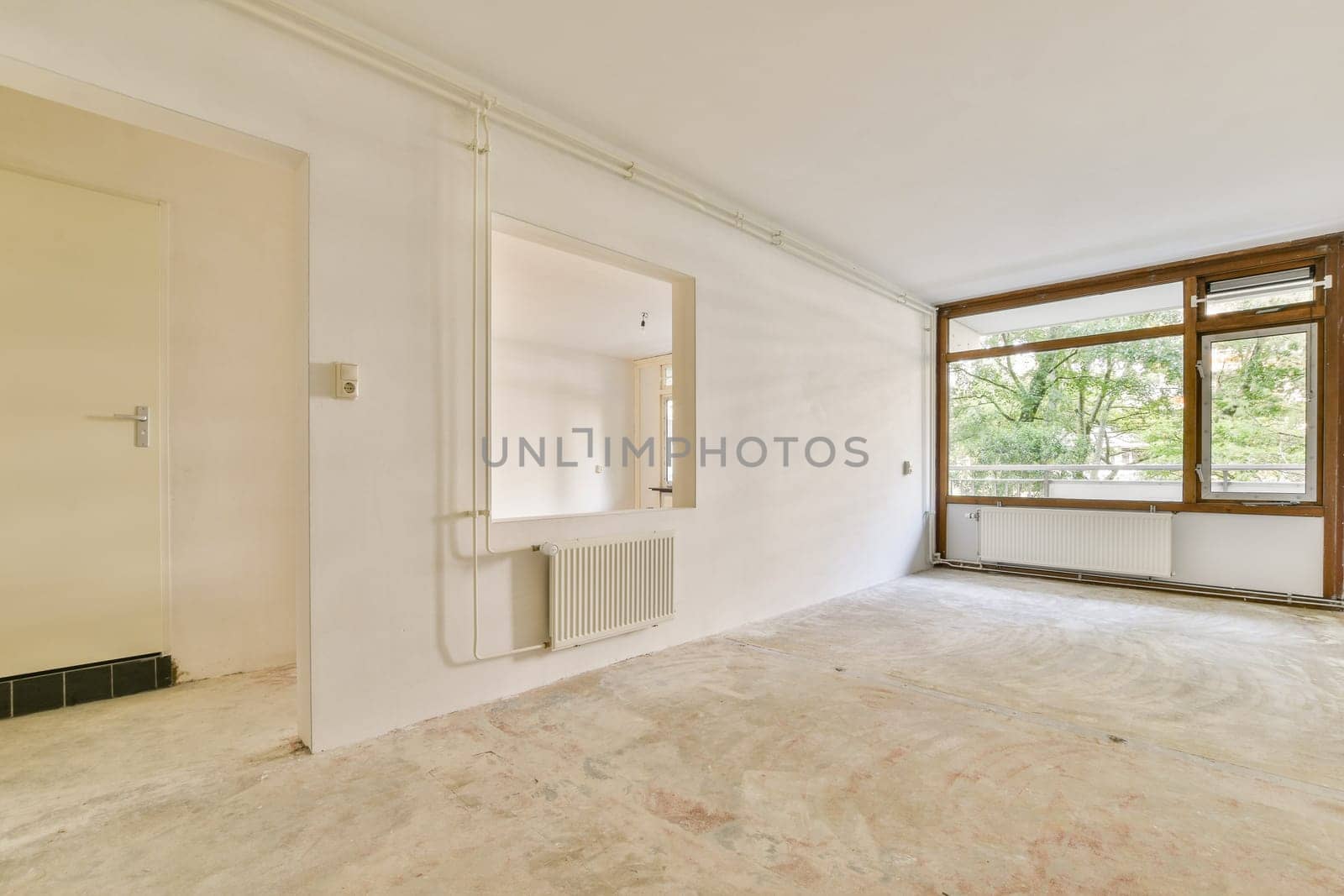 An empty, minimalist room featuring large windows that allow abundant natural light to flood in. The unfinished floor adds a sense of openness and potential.