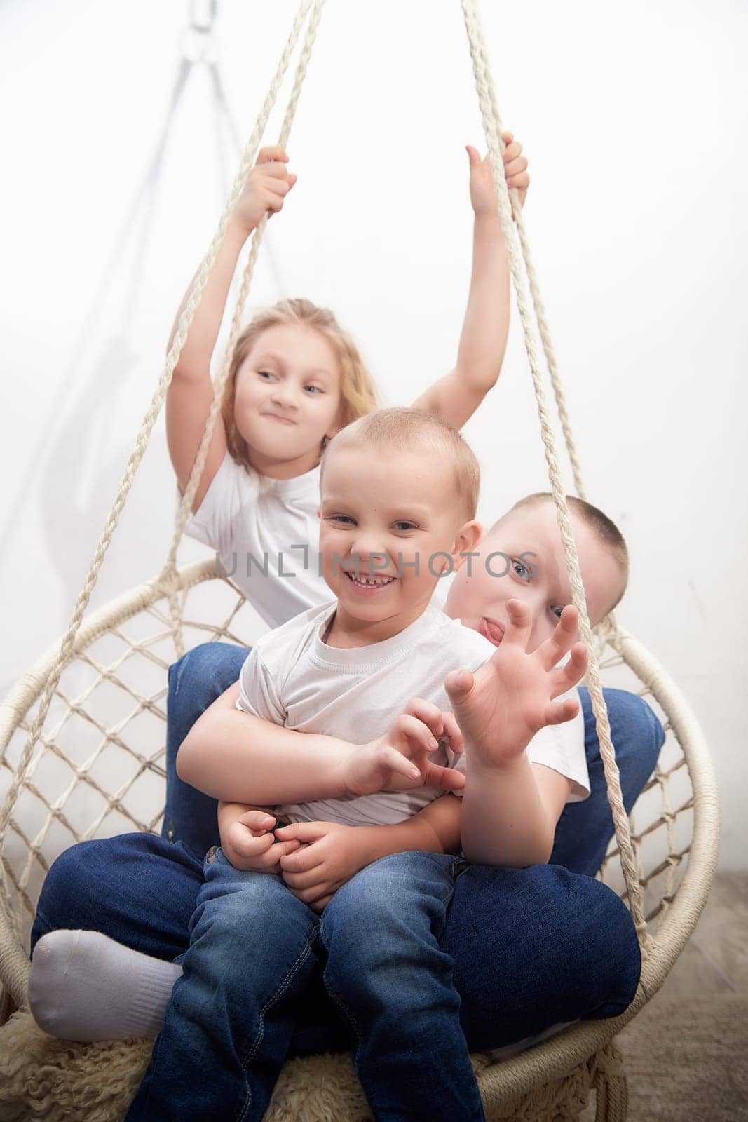 Three children happily play on a swinging seat, showcasing their friendship and cheer in a bright room with soft colors.