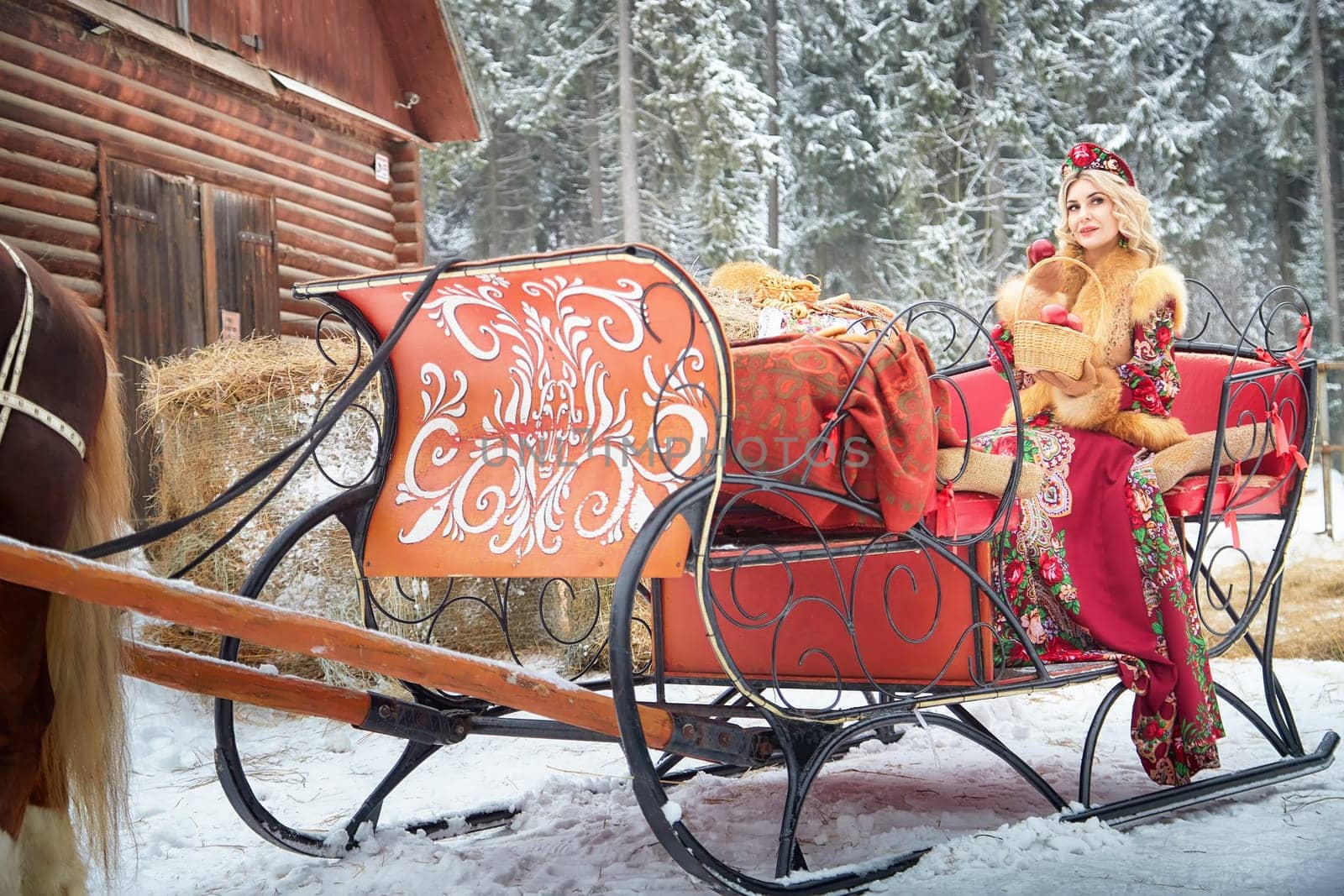 A gorgeous Russian girl in colorful attire poses with a horse during Maslenitsa, celebrating winter.