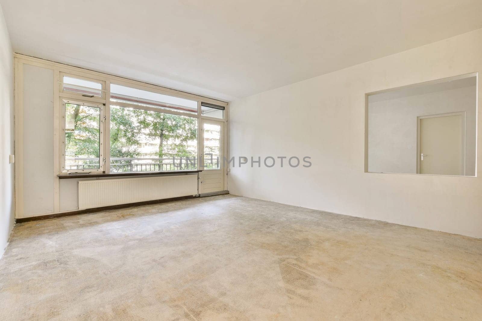 An empty room showcasing a minimalist design with large windows allowing natural light. The flooring and walls are simple, emphasizing space and openness.