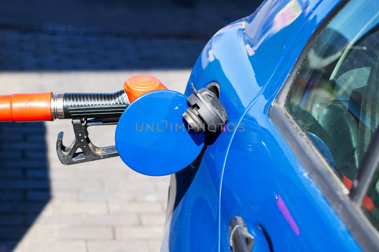 A blue car is currently being filled with gasoline at a busy gas station, ensuring it has enough fuel for its next journey ahead