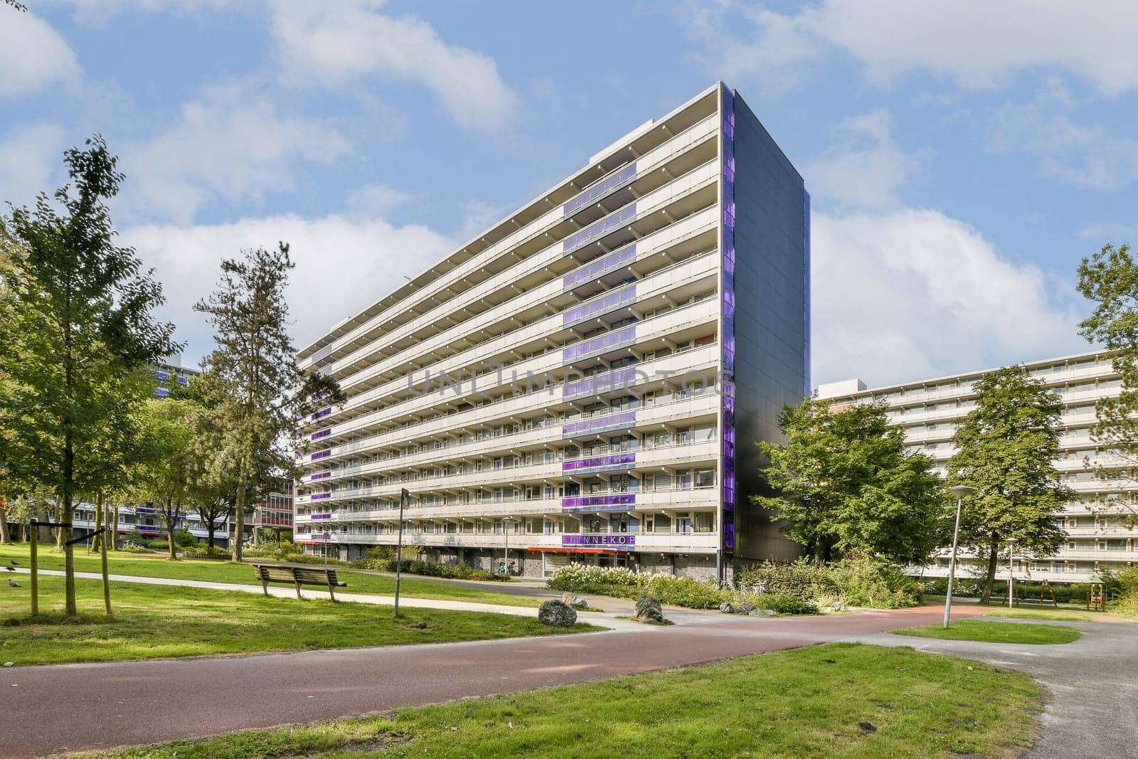 A striking modern residential building featuring multiple floors with large windows, set amidst beautifully landscaped greenery and pathways.