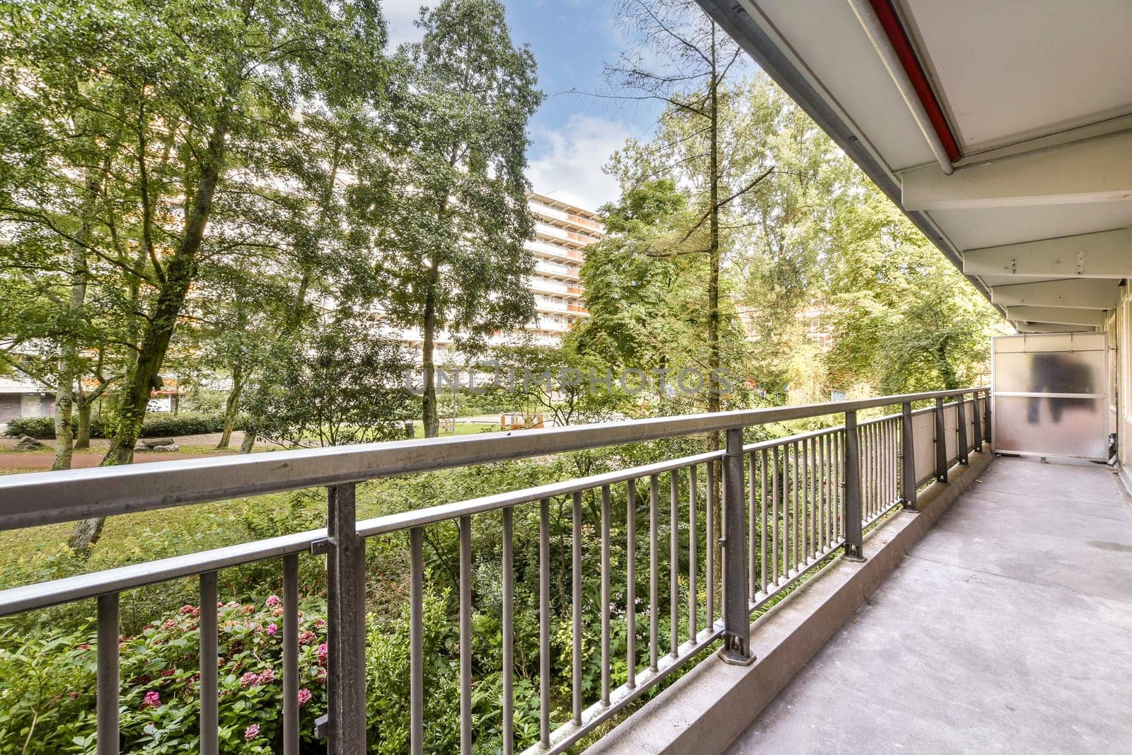 A well-maintained pathway through a modern urban park, flanked by greenery and residential buildings. The scene captures nature within an urban environment.