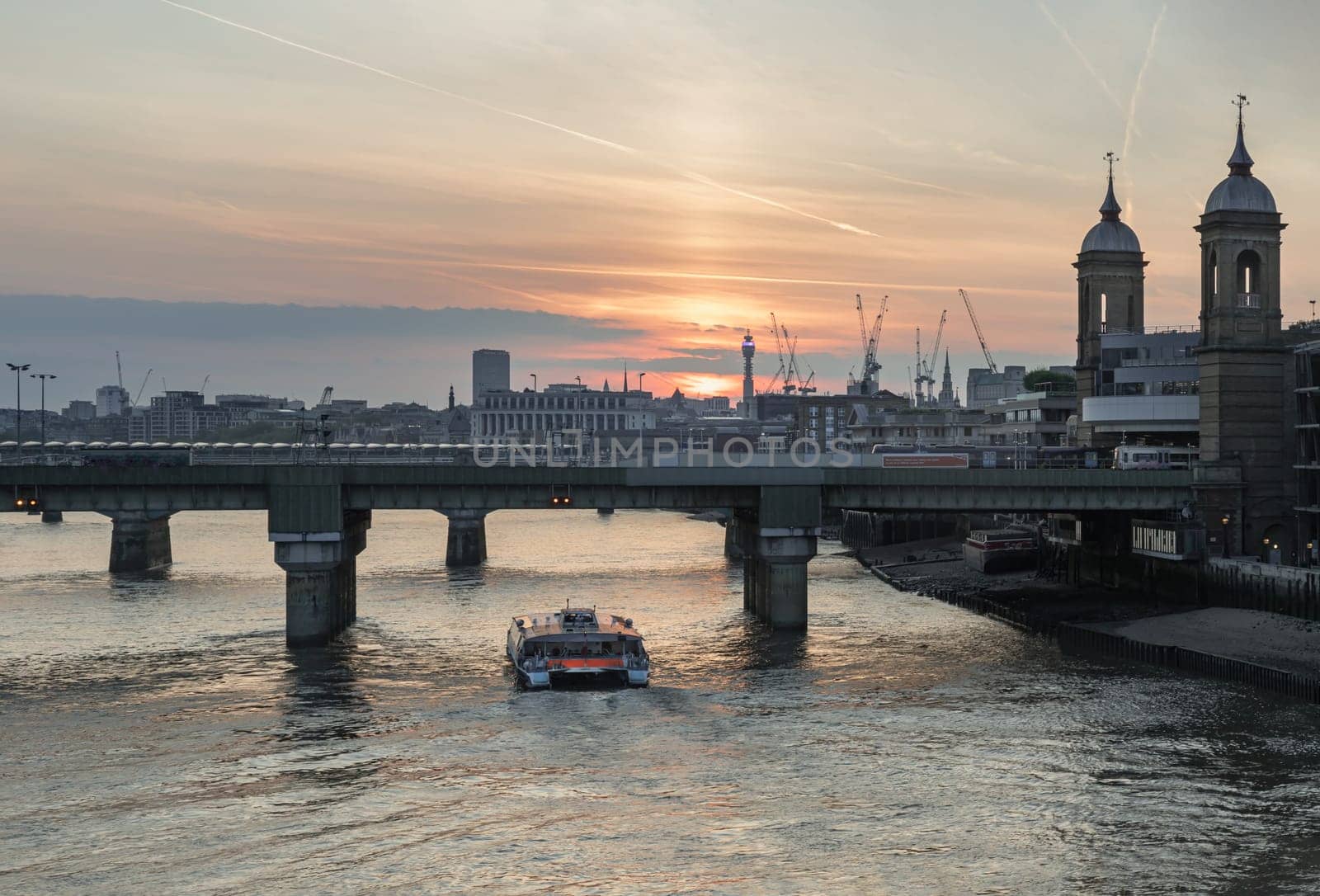 London, UK - Apr 27, 2025 - Amazing sunset view of Cannon street railway station bridge with Cruise boat on River thames and colour sky in the background. use it as your Wallpaper, Poster and Space for text, Selective focus.