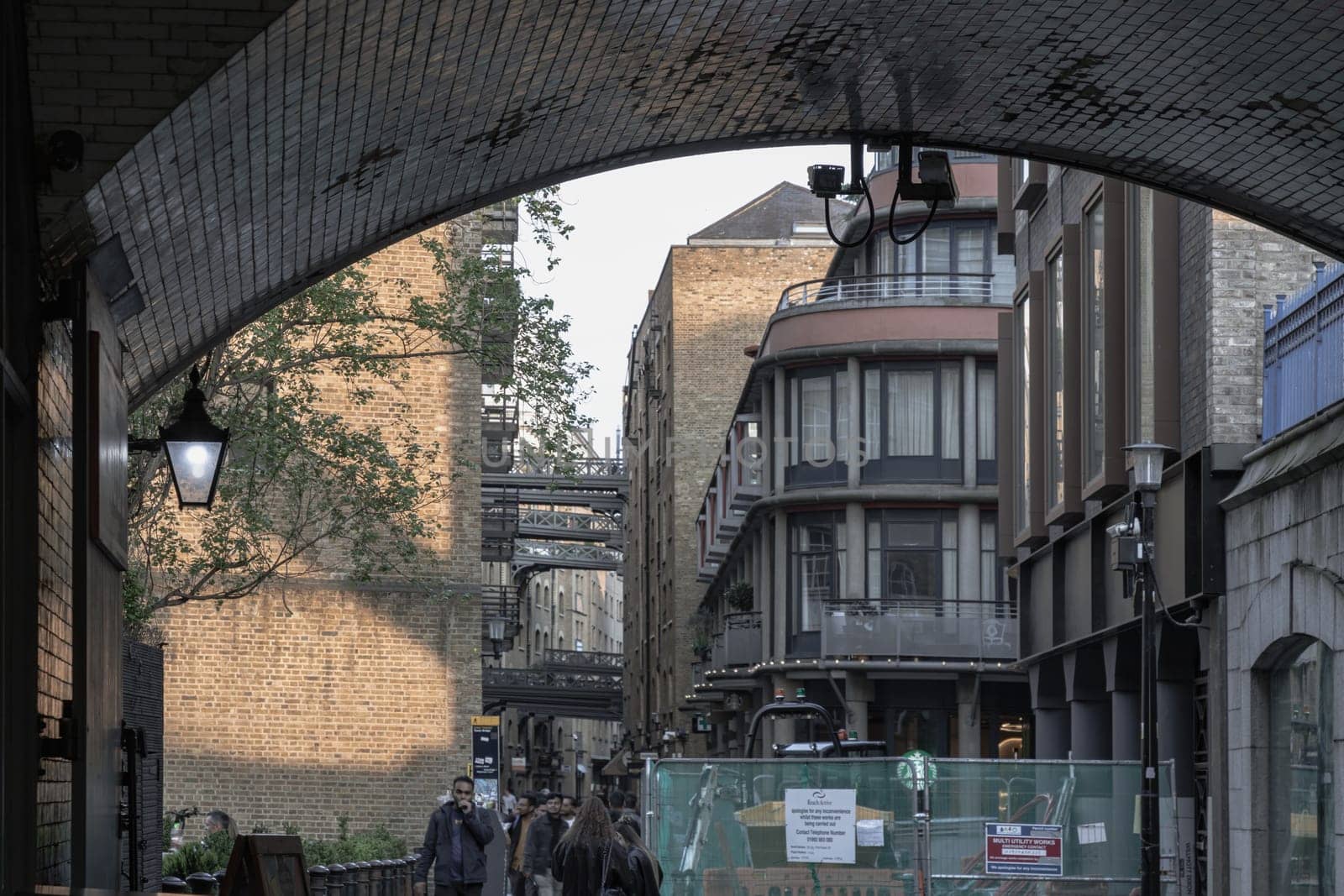 London, UK - Apr 27, 2025 - A view from under Tower Bridge, Pedestrians walking on Shad Thames is a historic riverside street alongside converted warehouse complex and shops under bridges in London. use it as your Wallpaper, Poster and Space for text, Selective focus.