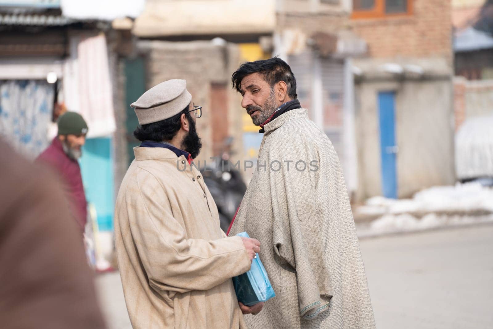 Srinagar, Kashmir - 4th Jan 2025: Group of elderly islamic men wearing traditional kashmiri Phiran and skull caps enjoying a cold winter morning in the market in Gulmarg