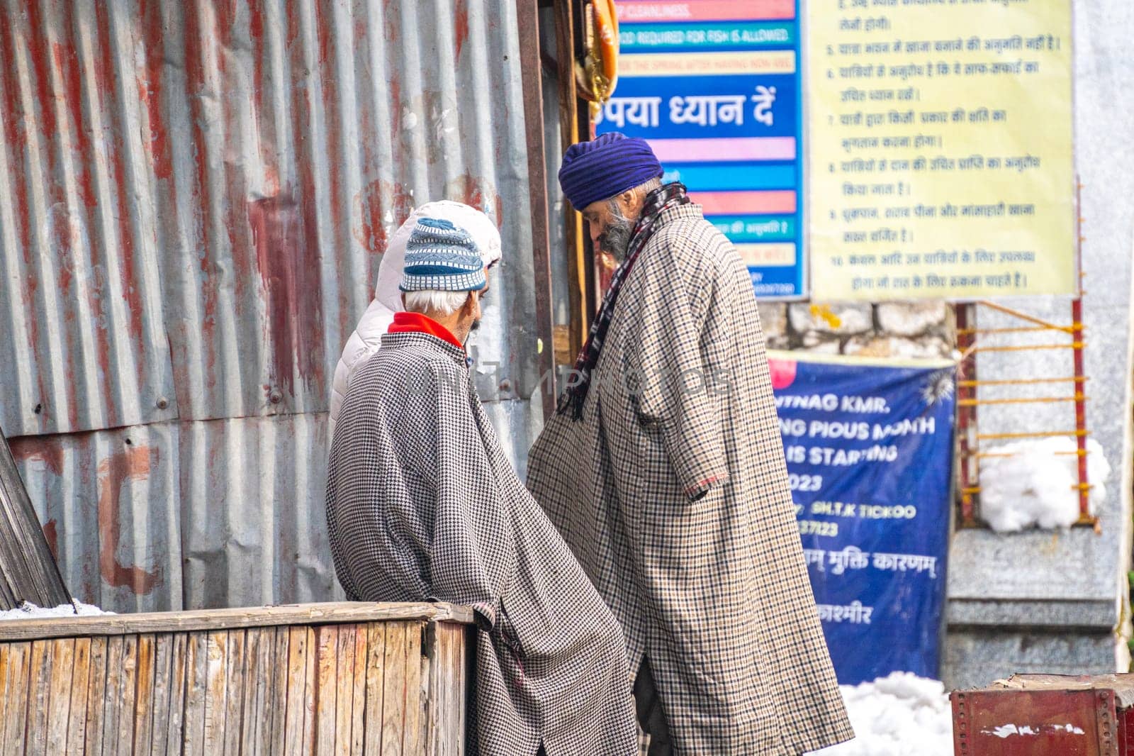 Srinagar, Kashmir - 4th Jan 2025: Group of men sitting on the side of the street engaging in conversation near the broken tin shed walls of a shop home in Kashmir
