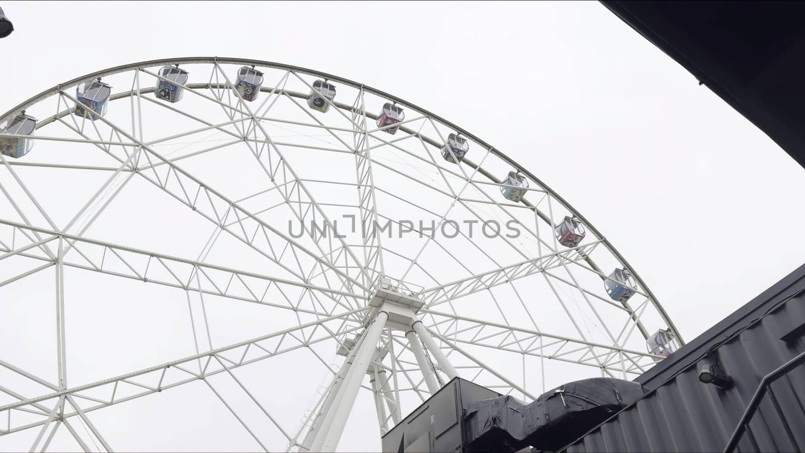 Ferris wheel rotating under cloudy sky near black building