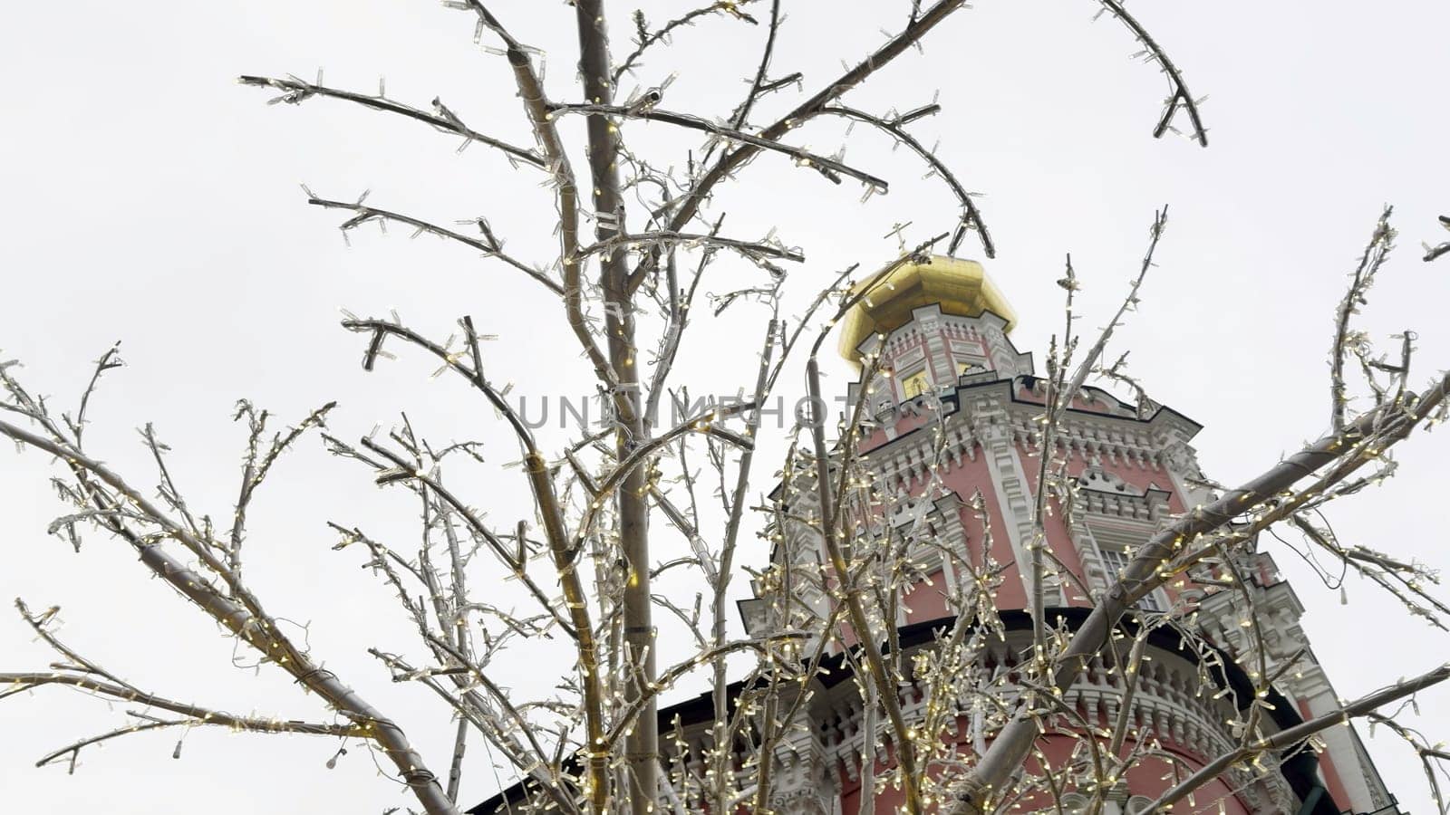 Christmas lights decorating bare tree branches in front of novodevichy convent bell tower in moscow, russia