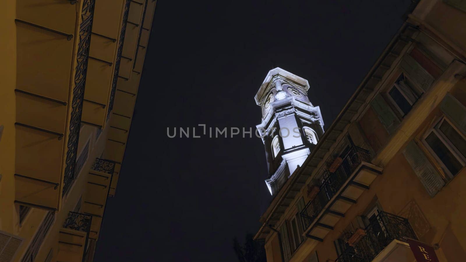 White bell tower standing tall against dark night sky, viewed from narrow street