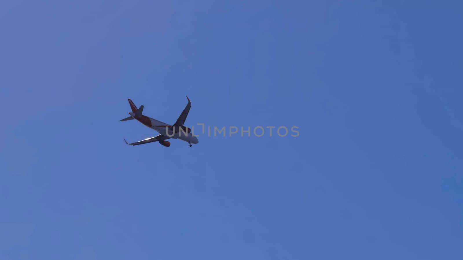 White and red passenger airplane is flying and turning in the clear blue sky