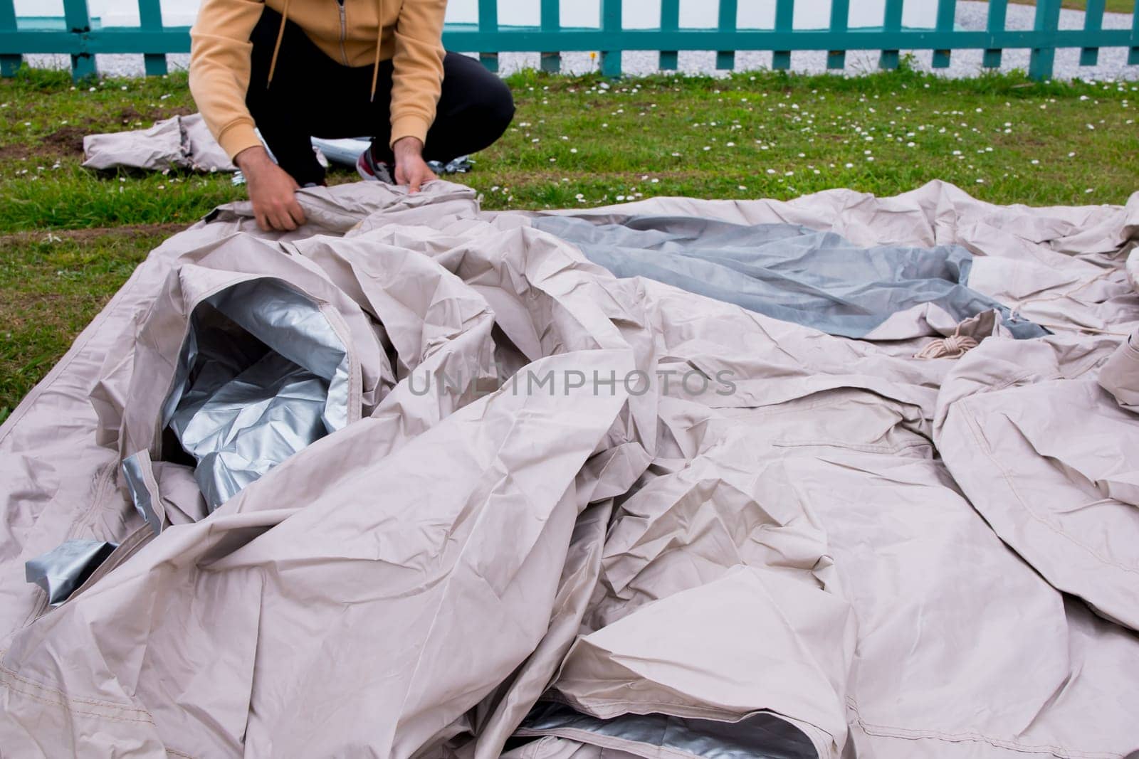 Young male setting up beige tent outdoors on green grass.