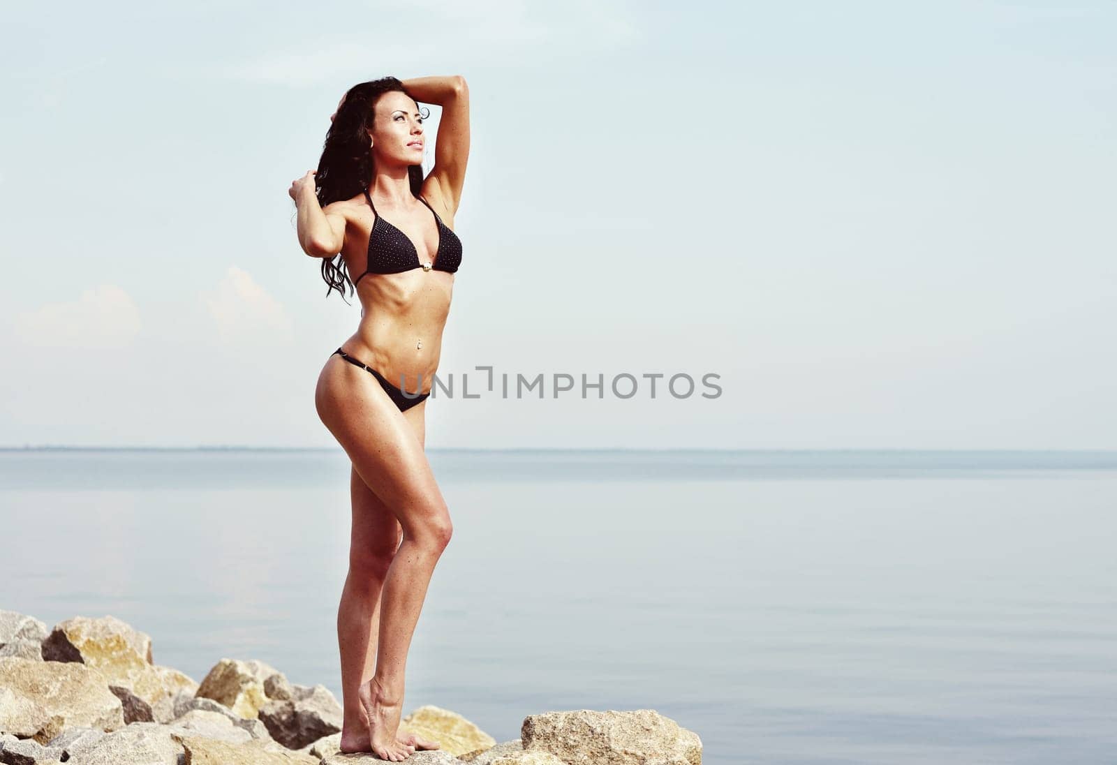 young woman in black bikini, sunbathing at sea shore
